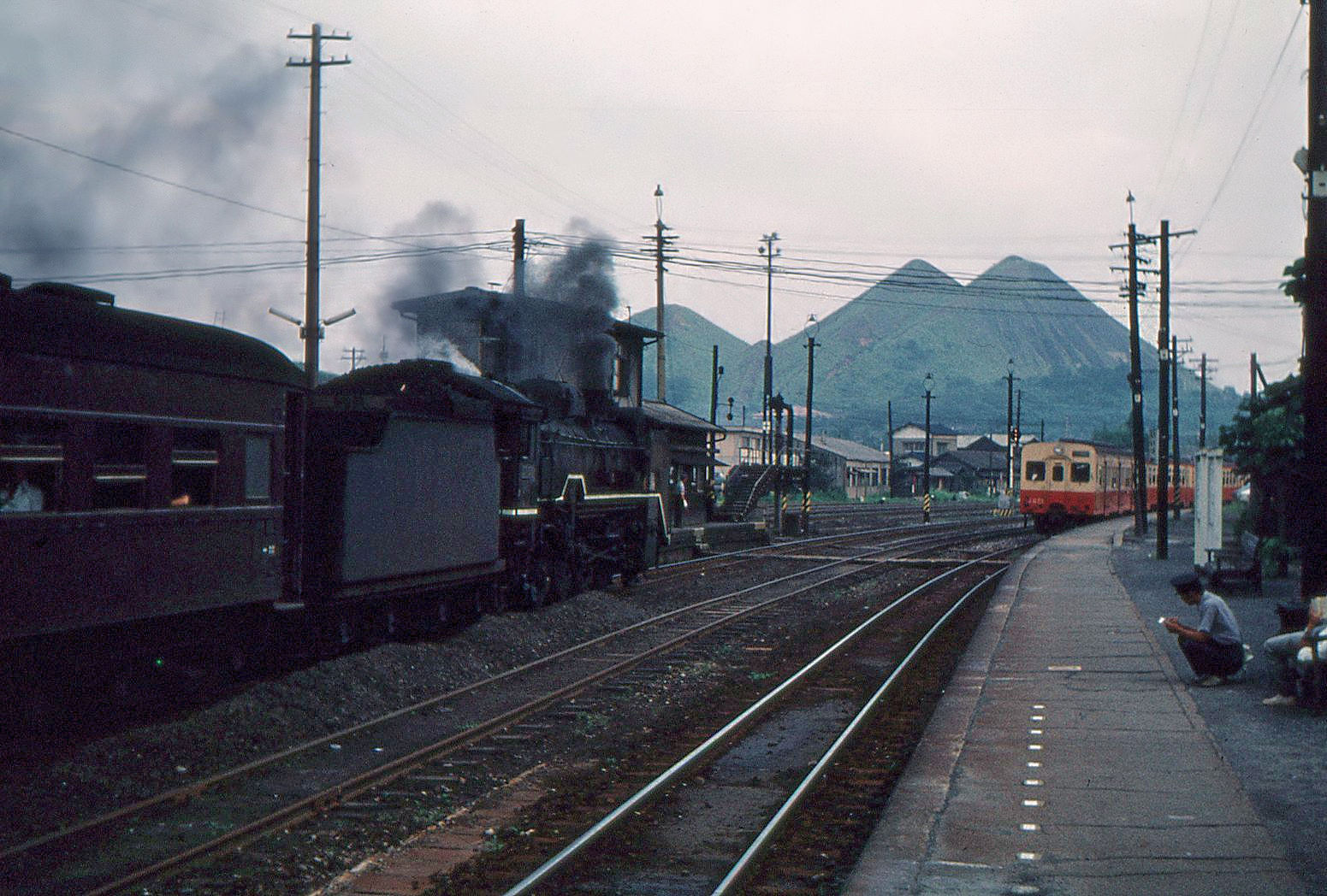 Das Chikuhô-Gebiet wie es früher war. Riesige Halden (Hochkippen), die vom Kohlebergbau stammen, davor ein (eher schmutziger) Dieseltriebzug und die Dampflok D51 542 mit uralten Wagen. Iizuka, 10.August 1972 