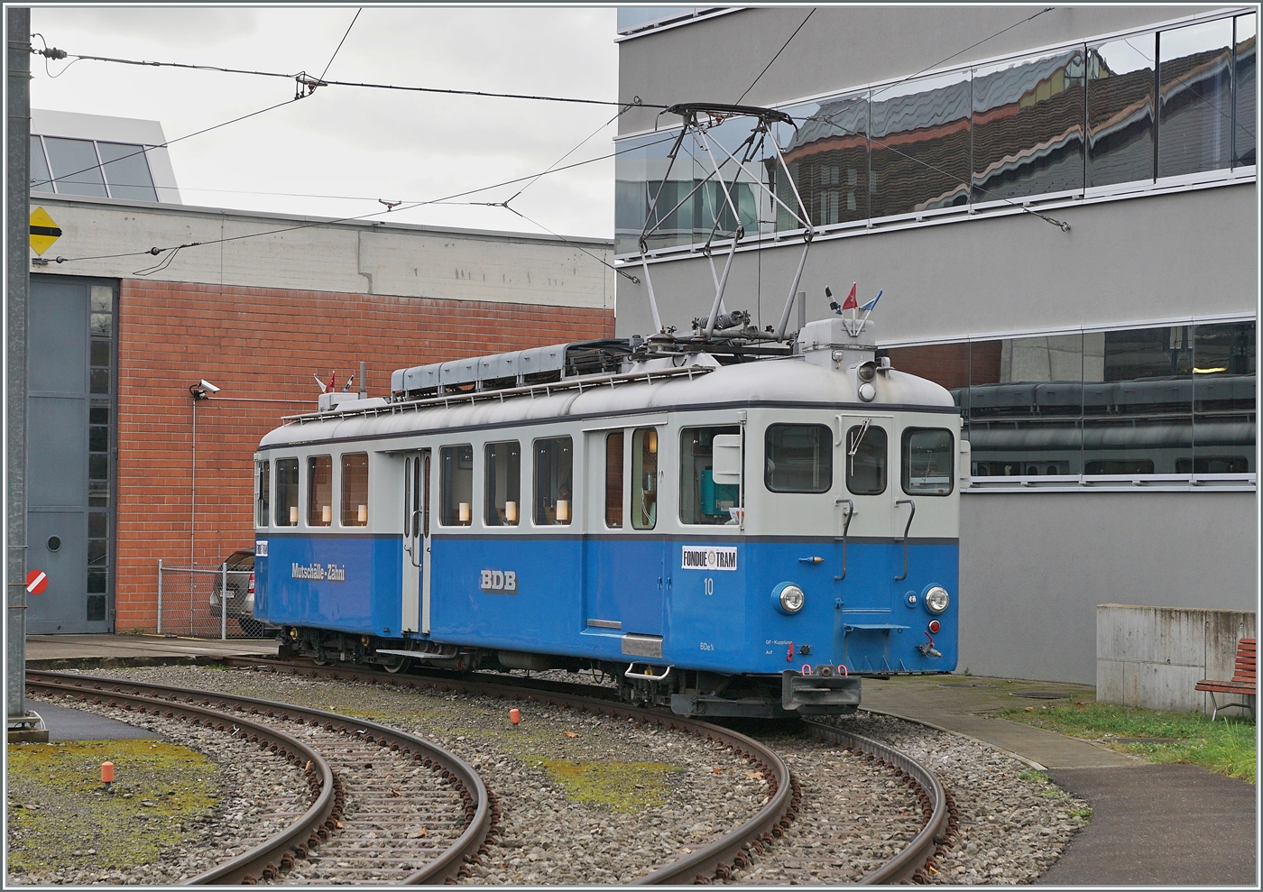 Der BD (Bremgarten-Dietikon Bahn) BDe 4/4 10 wurde im Jahre 1928 in Betrieb genommen. Gebaut hat dieser Triebwagen die Schweizerischen Wagonfabrik in Schlieren und die Maschinenfabrik Oerlikon, beide Werke sind nicht weit von der Bremgarten Dietikon Bahn entfernt im Limmattal bzw. bei Zürich. Der 16.22 Meter lange, 32 Tonnen schwere und 45 Km/h schnelle Triebwagen stand mit seinem Schwesterfahrzeug BDe 4/4 11 bis 1986 bei der BD im Einsatz. Während der BDe 4/4 11 mittlerweile ausrangiert wurde, konnte der BDe 4/4 10 zum Gesellschaftswagen umgebaut werden. Der heute als  Mutschälle-Zähni  im Sonderzug Einsatz stehende Triebwagen bietet in vielerlei Hinsicht einen geschätzten Beitrag im exklusiven Nostalgieverkehr und einen interessanten Gegensatz zum Planverkehr. Heute wartet das  Mutschälle-Zähni  auf den Einsatz als  Fondue-Tram  im Rahmen des bekannten Weihnachtsmarkts von Bremgarten.

(Fotostandpunkt: auf dem Bahnsteig)
6. Dezember 2024