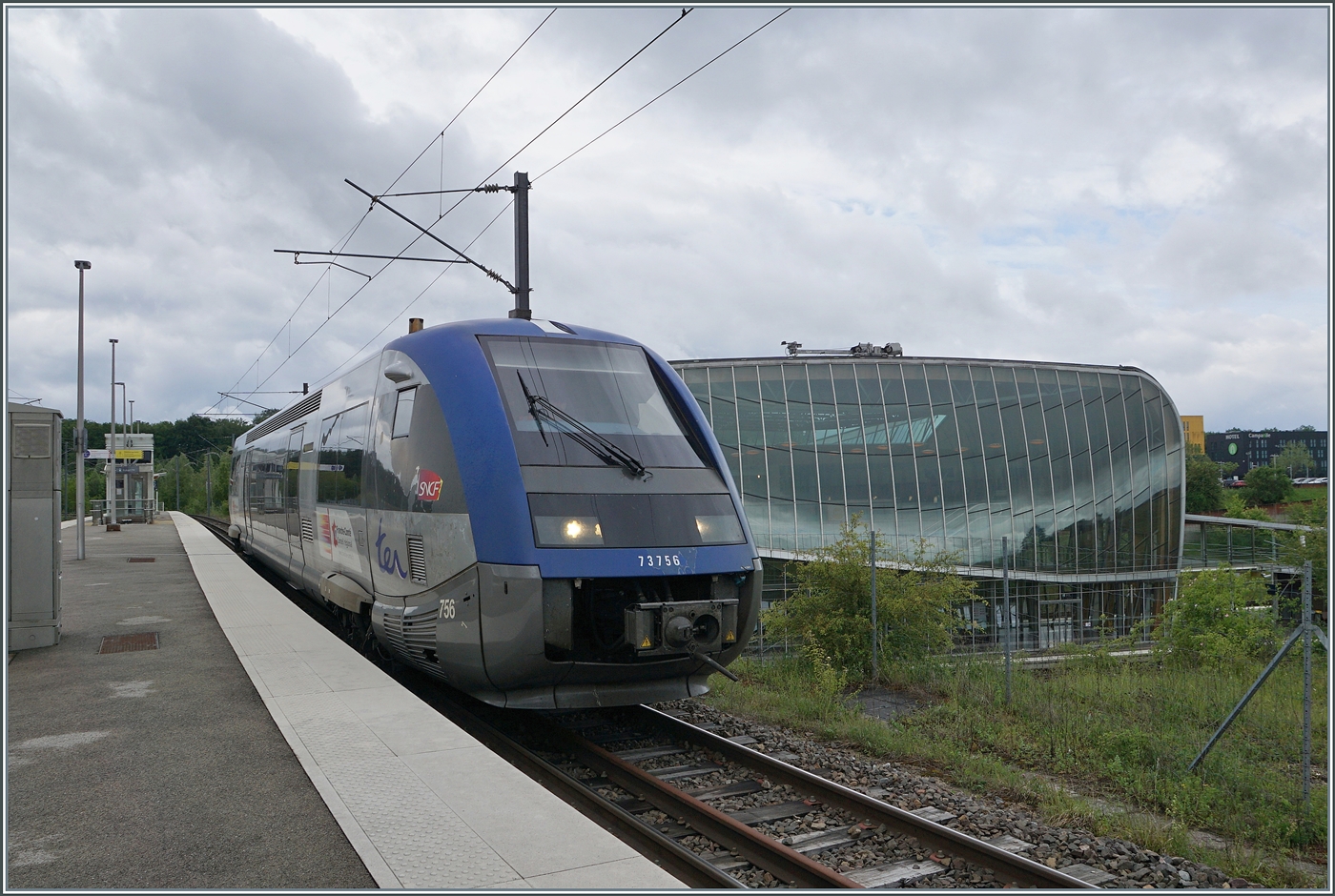 Der SNCF X 73756 verl�sst Meroux in Richtung Belfort. Im Hintergrund rechts im Bild ist das Empfangsgeb�ude der Bahnh�fe Meroux und Belfort-Montb�liard TGV zu sehen.

22. Mai 2026