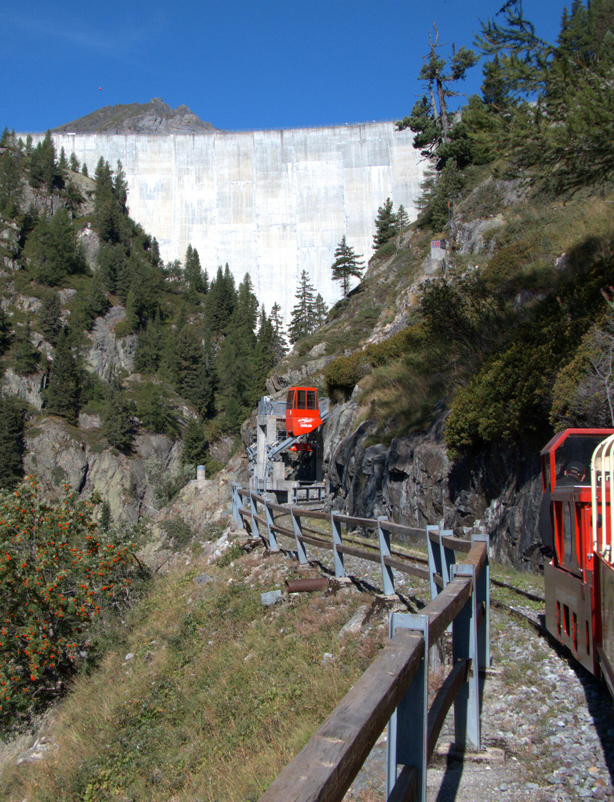 Der Umsteigebahnhof Pied du Barrage ist in Sicht, die rote Standseilbahn wartet auf die Fahrgäste vom Panoramazug. Im Hintergrund ein Teil der Staumauer des Lac d'Emosson. Lac d'Emosson, 25.8.2025