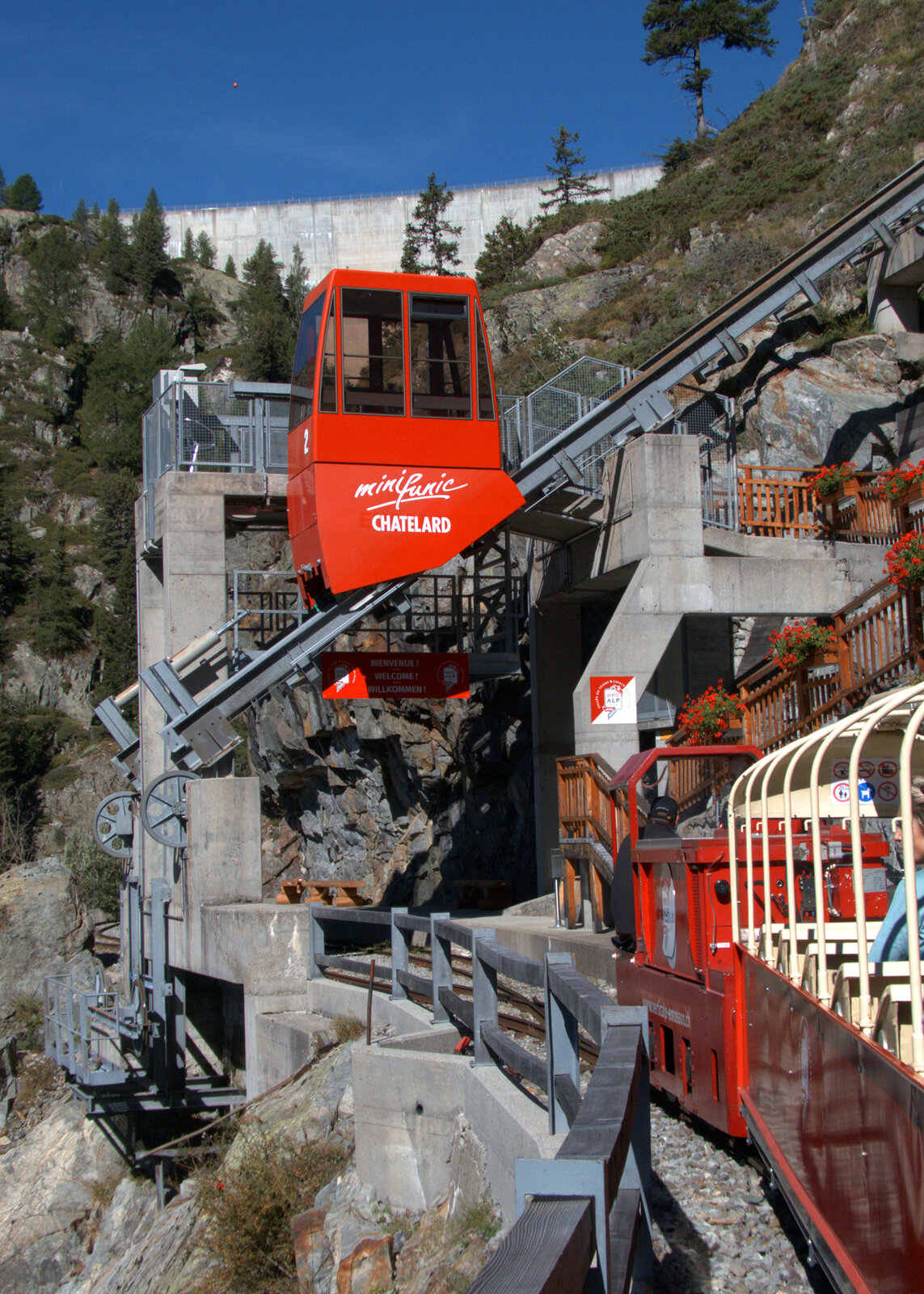 Der Umsteigebahnhof Pied du Barrage ist in Sicht, die rote Standseilbahn wartet auf die Fahrgäste vom Panoramazug. Im Hintergrund ein Teil der Staumauer des Lac d'Emosson. Lac d'Emosson, 25.8.2025