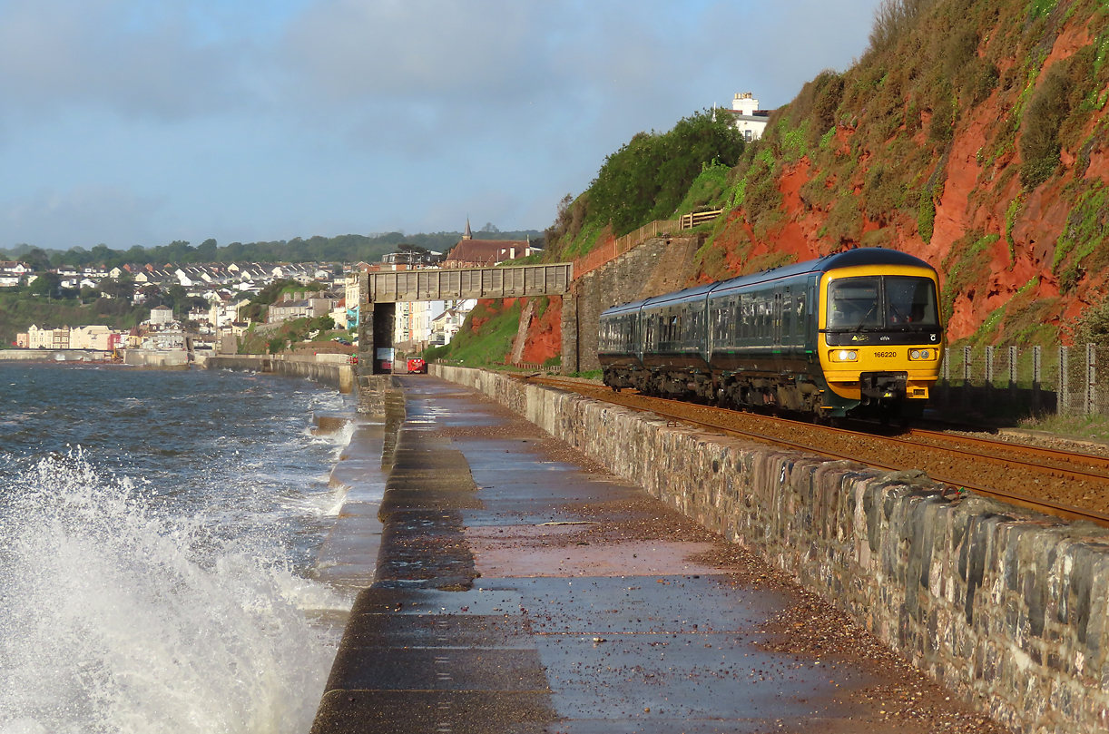 Der Wind am frühen Morgen peitscht hohe Wellen an das Festland: Lokalzug unterwegs vor schöner Kulisse nach Exeter. Dawlish, 18.5.2022