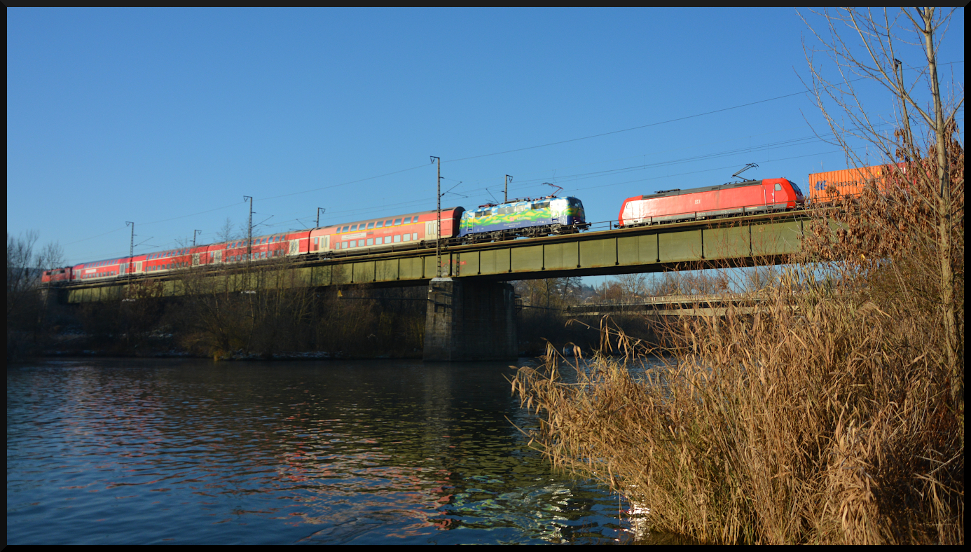 Die 111 074-1 (Touristik) mit dem Doppelstockzug von DB Gebrauchtzug und der 111 067-5 am 17.12.2022 als TRI-Ersatzzug für Go-Ahead Baden-Württemberg auf der Mainbrücke zwischen Heidingsfeld und Würzburg. Auf dem Gegengleis schiebt sich die 185 002-3 mit einem Containerzug langsam ins Bild.

