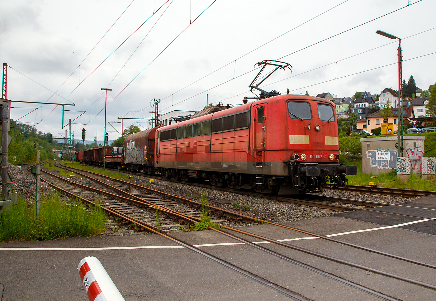 Die an die DB Cargo AG vermietete Railpool 151 002-3 (91 80 6151 002-3 D- Rpool) fährt mit einem gemischten Güterzug am 11.05.2023 durch Niederschelden (hier beim Bü 343 – km 112,183 der Siegstrecke) in Richtung Siegen.

Die Lok wurde 1973 von Krupp in Essen unter der Fabriknummer 5174, der elektrische Teil ist von AEG unter Fabriknummer 8820, gebaut, und an die Deutsche Bundesbahn geliefert. Bis zum 31.12.2016 gehörte sie zur DB Cargo AG. Zum 01.01.2017 wurden je 100 sechsachsige elektrische Altbau-Lokomotiven der Baureihen 151 und 155 an ein Konsortium aus dem Lokvermieter Railpool verkauft. Die DB Cargo mietet daraufhin 100 Loks von Railpool wieder an. Die anderen Maschinen werden dem freien Markt angeboten.

Diese sechsachsigen Loks (Co’Co’) sind immer noch starke Zugpferde, und so manche moderne Lok hat nicht diese Leistungsfähigkeit. Mit einer Stundenleistung von 6.288 kW (8.550 PS) bei 92 km/h und einer Anfahrzugkraft von 395 kN können diese Loks 3.000 t Züge bei 3 ‰ Steigung noch mit einer Dauergeschwindigkeit 75 km/h ziehen, bei 2.000 t Zügen sind es 100 km/h.
