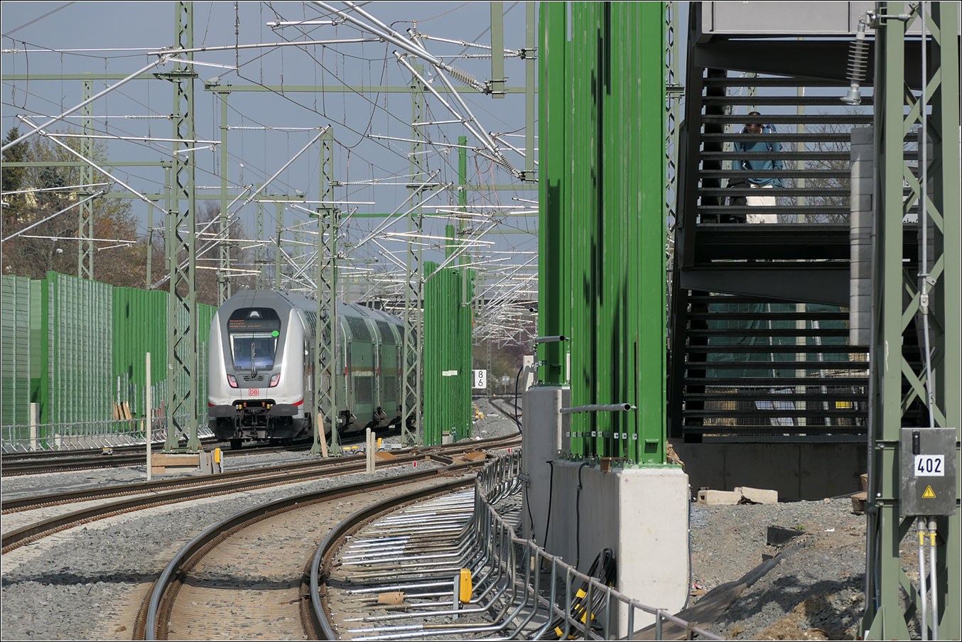 Die Bahn wird grüner - 

Von 2017 bis 2024 wurde die Main-Weser-Bahn im Abschnitt Frankfurt West - Bad Vilbel viergleisig ausgebaut um für die S-Bahn eigenen Gleise zu erhalten, was ein 15-Minuten Takt bis Bad Vilbel ermöglicht. In einem zweiten Bauabschnitt sollen die vier Gleise bis zum S-Bahn-Endpunkt Friedberg verlängert werden.

Erschrocken bin ich über die hohen Lärmschutzwände rechts und links der Bahn und teilweise auch zwischen den Gleisen. Einen Ausblick für die Fahrgäste gibt es da nicht mehr. Auch möchte ich nicht von meiner Wohnung auf solche Blickbarrieren blicken müssen. Wir selber wohnen an einer sehr stark befahren Strecke; die Zugvorbeifahrten empfinde ich nicht als störend.

Erkennbar im Bild auch der Nachteil von Fußgängerüberführungen gegenüber Unterführungen, da doch eine weit größerer Höhenunterschied überwunden werden muss. Dafür entfällt aber das oft unangenehme Raumgefühl in den Fußgängertunneln.

Aufgenommen an der S-Bahnstation Frankfurt-Eschersheim.

21.03.2024 (M)