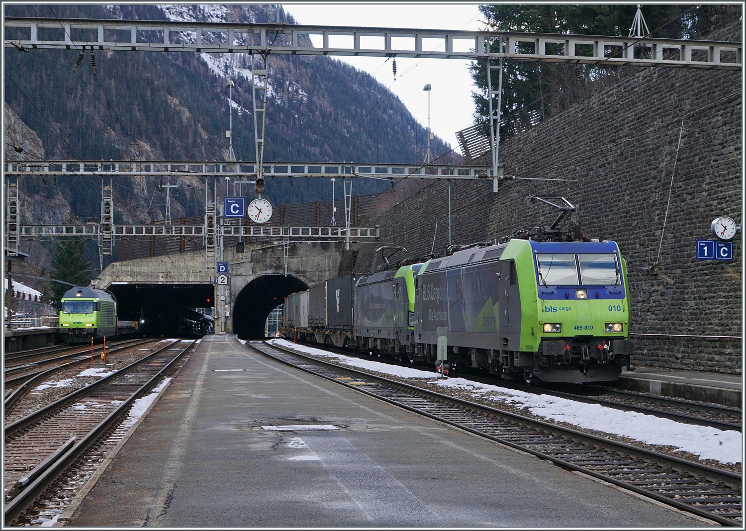 Die BLS Re 485 und eine BLS Re 475 fahren mit einem Güterzug in Richtung Norden durch den Bahnhof von engen Bahnhof von Goppenstein. Links im Bild erkennt man die  BLS Re 465 002 mit ihrem soeben aus Kandersteg angekommenen Autotunnelzuges (AT1), der in wenigen Minuten nach Kandersteg zurückfahren wird.

3. Jan. 2024