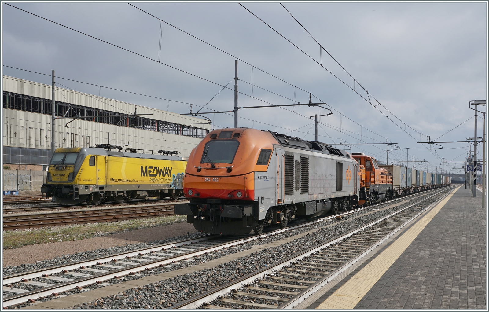 Die Dinazzano Pò (DPO) Eurolight D 284 002 (UIC 92 83 2284 002-8 I-DPO) hat sich in Reggio Emilia mit der D 744 006 (UIC 92 83 2744 006-3 IT-DPO) vor einen Güterzug gesetzt. Beachtenswert in der UIC Bezeichnung, dass die einerseits  I-DPO , andererseits  IT-DPO  verwendet wird. Ebenfalls erwähnenswert: die heutige DPO 284 002 wurde als Euro 4000 2010 in Berlin auf der InnoTrans gezeigt.  

14. März 2023
