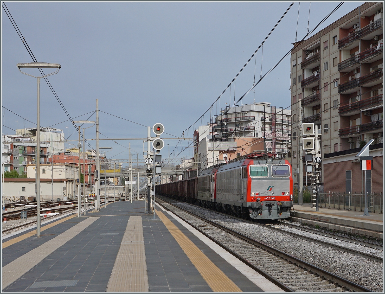Die FS Mercitalia E 652 048 und eine weitere fahren mit einem Güterzug aus vierachsigen offenen Güterwagen durch den Bahnhof von Barletta in Richtung Süden. 

25. April 2023