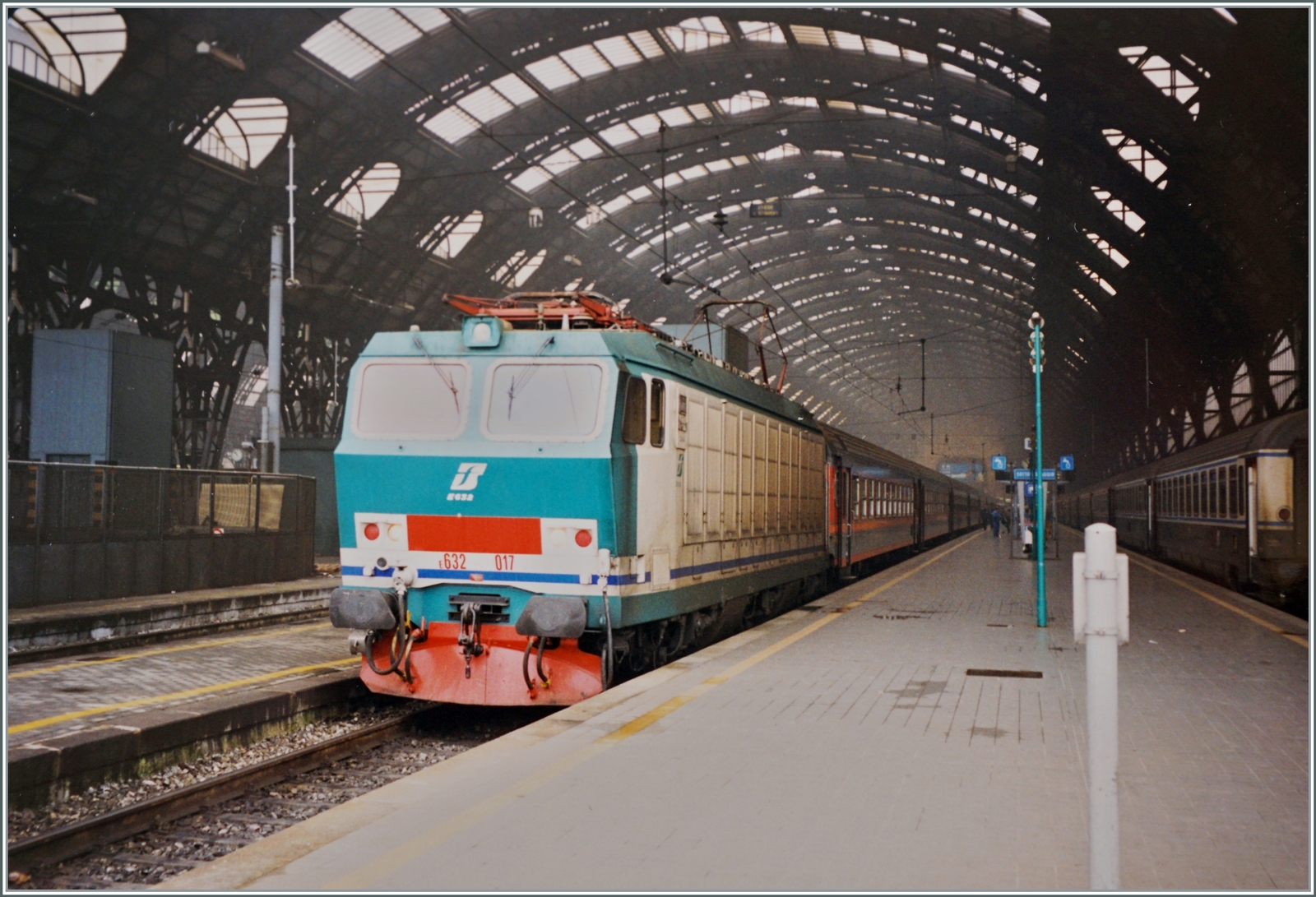 Die FS Trenitalia E 632 017 trägt die nicht ganz so überzeugende, damals neue Farbgebung  Verde/Bianca . Die Lok wartet mit einem Eilzug in Milano auf die Abfahrt nach Torino Porta Nuova. 

Analogbild vom Februar 1999 