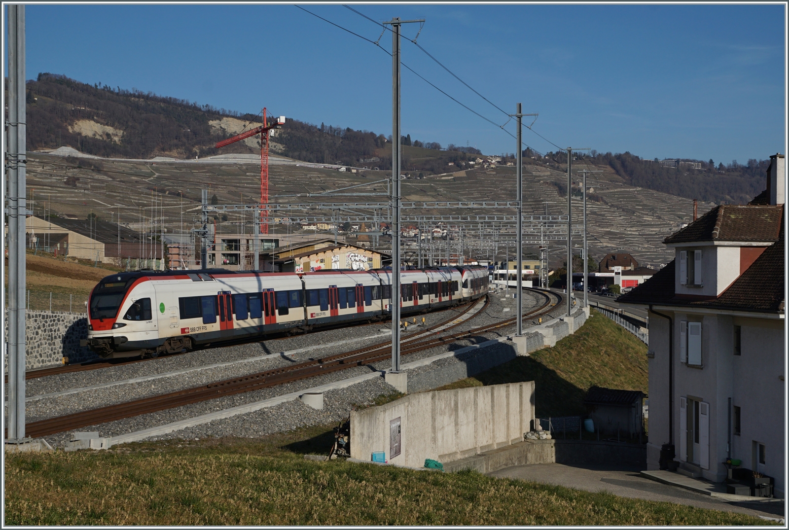 Die gleiche Szene aus einem anderen Blickwinkel: Um den RER Vaud S-Bahnen das Wenden in Cully zu ermöglichen und damit die Frequenzen in der Agglomeration Lausanne zu erhöhen, hat man den Bahnhof umgebaut: das bergseitige Gleis im Einfahrbereich etwa gestreckt und gegen den Berg verschoben, das ehemalige Durchfahrgleis hat nun Seite Lausanne Weichenverbidnungen ohne den Gengenverkehr zu beeinträchtigen, zudem ist das ehemalige Überholgeleis 3 nun das Durchfahrtgleis Richtung Lausanne. 
Zwei SBB RABe 523 erreichen als  RER Vaud Cully auf Gleis 2, Endstation. Der Zug wendet hier. 

20. Februar 2023