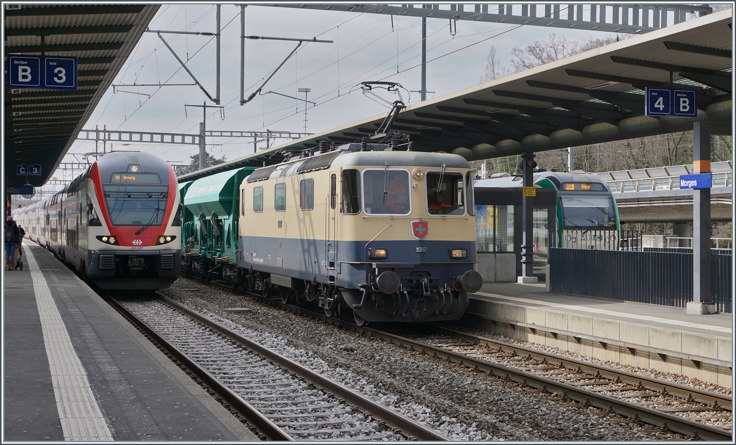 Die IRSI/IGE  Rheingold  Re 4/4 II 11387 (Re 421 387-2) im Dienste der BAM MBC ist mit ihrem Kieszug von Gland in Morges angekommen. Auf Gleis 3 erreicht der SBB RABe 511 037 als RE33 nach Vevey den Bahnhof von Morges.

4. März 2024