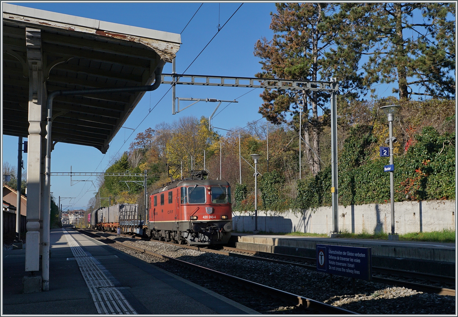 Die SBB Re 4/4 II 11240 (Re 420 240-4 ) fährt mit einem kurzen, aber bunten Güterzug durch den Bahnhof von Burier, welcher noch immer über sein altes Bahnsteigdach verfügt, wie links im Bild andeutungsweise zu sehen ist. 

23. November 2023