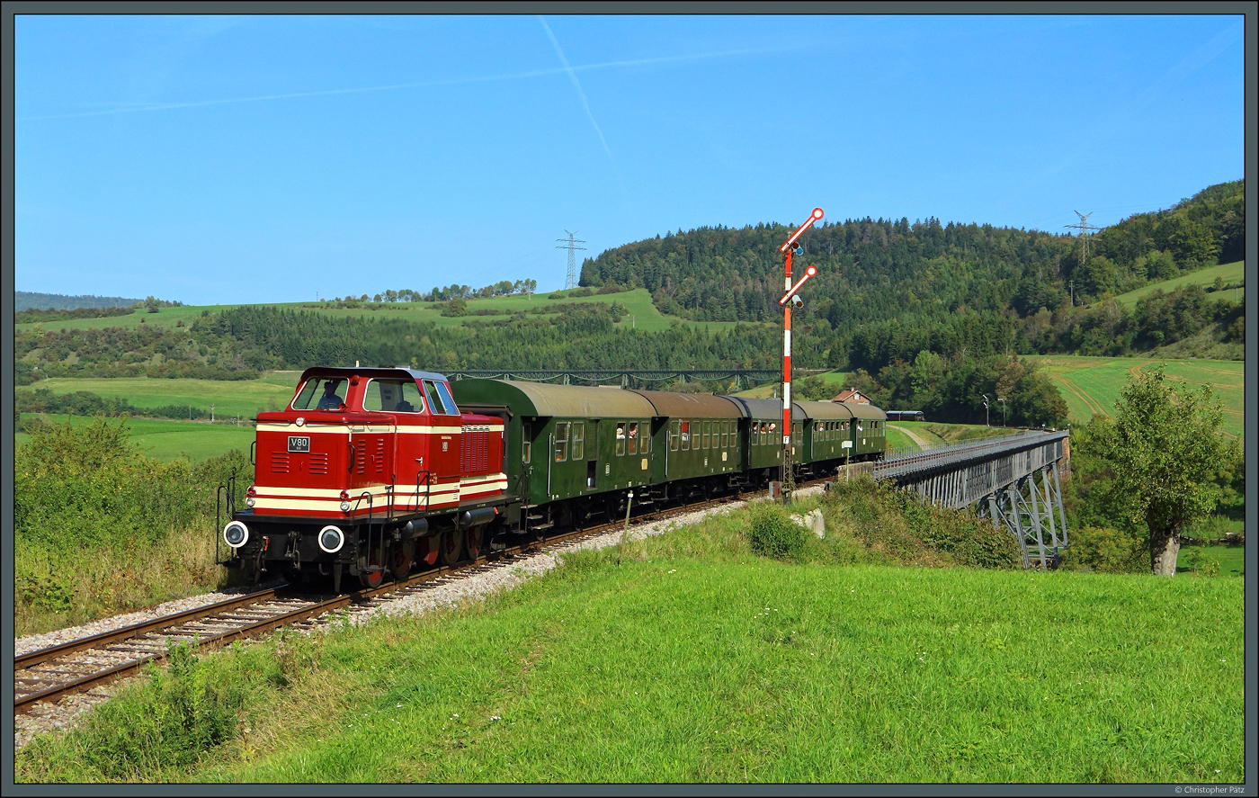 Die V80 BB (265 401) der Bahnbetriebe Blumberg hat am 02.10.2023 mit dem Zug 32 den (durchgeschaltenen) Bahnhof Epfenhofen verlassen und passiert dessen Einfahrsignal. Damit hat der Zug auch den Epfenhofener Viadukt berquert. Nach einigen Minuten und einem weiten Bogen um den Ort Epfenhofen wird der Zug den im Hintergrund sichtbaren Biesenbach-Viadukt befahren.