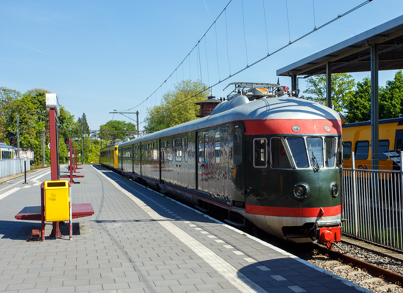 Die zweiteilige  Muizeneus  (Mausnase), der zweiteilige Elektrotriebwagenzug Mat '46 – NS 273, am 29 April 2025 im Het Spoorwegmuseum (bis 2005 NSM - Nederlands Spoorwegmuseum / Niederländischen Eisenbahnmuseum) in Utrecht im Bahnhof Maliebaanstation. Ein sehr schönes Eisenbahnmuseum das zum Verweilen einlädt, leider fehlte uns dieses Mal die Zeit dafür. Übrigens das Gleis 2 (nebenan) ist noch ein aktives Bahngleis, hier fährt stündlich der Pendelzug (als RE) von Utrecht Centraal ein bzw. aus. 

Der ET Mat '46 – NS 273 (Typ ElD2) wurde 1952 von der Werkspoor N.V. in Utrecht für die NS - Nederlandse Spoorwegen (Niederländischen Staatsbahnen) gebaut und geliefert. Die elektrische Ausrüstung ist von Heemaf. 

Die NS-Baureihe Mat ’46 oder Materieel ’46 war eine Serie von 144 Elektrotriebzügen (davon 79 zweiteilige ELD2 und 65 vierteilige ELD4), die von der NS - Niederländischen Staatsbahnen ab 1948 eingesetzt wurde. Offiziell wurden diese Züge auch als Plan A, AB, B und C bezeichnet. Inoffiziell wurde auch die Bezeichnung „Mäusenase“ verwendet. Den Spitznamen Muizeneus verdanken sie den ab den 1960er Jahren bemalten gelben „Schnurrbart“. Die Mat ’46 blieben bis in die 1980er Jahre als Eil- und Schnellzug in Betrieb. 

Die Serie baute auf früheren stromlinienförmigen Typen auf, die ab 1936 in den Niederlanden in Gebrauch kamen. Diese Serien, mit denen die Mat '46 in mehreren Einheiten gekoppelt werden konnten, waren als Mat '35, Mat '36 und Mat '40 bekannt. Da im Zweiten Weltkrieg ein Großteil der niederländischen Eisenbahnausrüstung verloren ging, herrschte nach der Befreiung ein großer Mangel an Ausrüstung. Um diesen Mangel zu beheben und Ausrüstung für die weitere Elektrifizierung des Eisenbahnnetzes zur Verfügung zu haben, wurden neue Triebzüge angeschafft. Zwischen 1948 und 1952 wurden 65 vierteilige Züge (NS 641–705) und 79 zweiteilige Züge (NS 221–299) in Betrieb genommen. Technisch und auch optisch waren die Mat '46 dem Mat '36 fast gleich.

Die Vier-Wagen-Garnituren bestanden aus zwei fest gekoppelten Zwei-Wagen-Garnituren mit je einem Steuerstand an beiden Enden der Zuggarnitur. Dieser war nach heutigen Maßstäben nicht besonders komfortabel. Die Steuerstandkabine war so eng, dass der Lokführer seinen Sitz (der einem Fahrradsattel ähnelte) hochklappen musste, bevor er seinen Platz verlassen konnte.

Jeder Zwei-Wagen-Satz hatte ein Jacobs-Drehgestell, als ein gemeinsames Mitteldrehgestell. Die Vier-Wagen-Garnituren hatten somit zwei Jacobs-Drehgestelle. Dies führte zwar zu einer Gewichtsersparnis, hatte jedoch einen eher unruhigen Lauf zur Folge, da Querkräfte von einem Wagenkasten auf den anderen übertragen wurden. Ein Zwei-Wagen-Zug wog 89 Tonnen, ein Vier-Wagen-Zug wog 169 Tonnen. Die Leistung betrug 796 kW bzw. 1.592 kW. Zwar waren Geschwindigkeiten bis zu 140 km/h zulässig, im Normalfahrplan wurden jedoch 125 km/h meist nicht überschritten. Die elektrischen und pneumatischen Verbindungen in den automatischen Scharfenberg-Kupplungen ermöglichten den Betrieb der Garnituren in Mehrfachtraktion mit den Zuggarnituren Mat '35, Mat '36, und den später gelieferten Mat '54.

Ursprünglich waren die Züge olivgrün mit roten Streifen (wie hier), ab den 1960er Jahren wurden sie dann grasgrün mit einem gelben „Schnurrbart“ auf der Nase. Der ursprüngliche Plan, alle Sets gelb zu streichen, wurde nie verwirklicht. Lediglich vier zeiteilige Züge (279, 281, 295 und 299), wurden ab etwa 1970 in der neuen NS-Hausfarbe gelb lackiert. Im Gegensatz zum „Hondekoppen“ (Mat ’54) waren die Züge nie mit einem zentralen Türverschuss ausgestattet, so mussten die Schaffner die Türen an jeder Station manuell schließen.

Am 24. September 1983 fuhr der Zug 676 als Abschiedszug zwischen Haarlem und IJmuiden hin und her. Einen Tag später gehörten sowohl der Einsatz der Mat '46, als auch der Zugverkehr auf der Bahnstrecke Santpoort Noord – IJmuiden der Vergangenheit an.

Nach der Stilllegung:
Nachdem im September 1983 der letzte 46er aus dem regulären Personenverkehr verschwand, wurden noch drei Zwei-Wagen-Garnituren für Test- und Unterrichtsfahrten eingesetzt. Die Züge 279, 285 und 291 waren noch mehrere Jahre im niederländischen Eisenbahnnetz im Einsatz. Der gelbe Triebzug 279 hielt sogar bis 1990 durch und wurde 1992 endgültig verschrottet.

Schließlich ist der Triebzug 273 der Einzige, der in der Sammlung des Niederländischen Eisenbahnmuseums in Utrecht erhalten geblieben ist. Dieser Triebzug wurde Mitte der 1990er Jahre restauriert, erhielt wieder seine ursprüngliche Farbgebung und wird heute für Sonderfahrten eingesetzt.

Technik der zweiteiligen ET (ELD2):
Die zweiteiligen Zuggarnituren sind 44,7 Meter lang und wiegen bei der Anlieferung 89 Tonnen. Ein Triebzug ist mit 4 Elektromotoren des Herstellers Heemaf vom Typ TM 711 (max. Leistung 199 kW (270 PS), 320 A, 1.380 U/min und Dauerleistung 155 kW, 250 A, 1,550 U/min) ausgestattet. Diese Leistung steht bei einer Stundenbelastung von 320 Ampere und einer Spannung von 675 Volt zur Verfügung. Insgesamt verfügt ein Triebzug über eine Leistung von 796 kW (1.080 PS). Die Aufhängung dieser Motoren entspricht der Aufhängung einer Straßenbahn. Der Fahrmotor ist einseitig gleitgelagert auf der Achse gelagert. Der Antrieb der Motorwelle erfolgt über ein Ritzel, dass das Zahnrad auf der Radsatzwelle antreibt. Der Zug ist für eine Geschwindigkeit von 140 km/h ausgelegt. Im normalen Zugbetrieb wurde eine Geschwindigkeit (Planmäßig) von 125 km/h gefahren. Der Zug verfügt über 24 Sitzplätze der zweiten Klasse und 80 Sitzplätze der dritten Klasse. Der Zug ist außerdem mit 21 Klappsitzen ausgestattet. Mit der Abschaffung der 3. Wagenklasse 1956 wurde aus der 2. Klasse die 1. Klasse und aus der 3. Klasse die 2. Klasse.

Die Pressluft für die Druckluftbremse und verschiedene elektropneumatische Geräte wird von zwei Kompressoren, die sich unter dem Fahrgestell befinden, erzeugt. Sie liefern bis zu 280 Liter Luft pro Minute. Zur Stromversorgung des Steuerstroms und der Beleuchtung ist unter dem Wagen ein Motorgenerator von Heemaf vom Typ GM32/30 (Dauerleistung 10 kVA, 1500/100 V DC, bei 2.000 U/min), installiert. Dieser wandelt die 1.500 Volt Oberleitungsspannung in 100 Volt Spannung für den Steuerstrom und 145 Volt für die Beleuchtung um. Unter dem Wagen befinden sich die Schaltschränke und Relaiskästen. Auch Anfahrwiderstände, Fahrschalter und die Folgerolle finden unter dem Wagen Platz. Die Wagen sind mit je einem Scherenstromabnehmer von BBC über den Wagenkasten ausgestattet. Um zu verhindern, dass zu viel Strom durch den Zug fließt, wurde auf dem Dach des Zuges eine 1.000-Ampere-Sicherung angebracht. Die Bezeichnung der Triebzüge lautet ElD2. Die Achsfolge ist Bo'(2')Bo'.

Technik der vierteiligen ET (ELD4):
Die vierteiligen Zuggarnituren sind 87,8 Meter lang und wiegen bei der Anlieferung 169 Tonnen. Die Endwagen (mit Führerstand) haben jeweils eine Länge von 22,09 Metern und die Mittelwagen haben eine Länge von 20,69 Metern. Ein Triebzug ist mit 8 Elektromotoren des Herstellers Heemaf vom Typ TM 711 (max. Leistung 199 kW (270 PS), 320 A, 1.380 U/min und Dauerleistung 155 kW, 250 A, 1,550 U/min) ausgestattet. Insgesamt verfügt ein Triebzug über eine Leistung von 1.592 kW (2.160 PS). Die Aufhängung dieser Motoren entspricht der Aufhängung einer Straßenbahn. Der Fahrmotor ist einseitig gleitgelagert auf der Achse gelagert. Der Antrieb der Motorwelle erfolgt über ein Ritzel, dass das Zahnrad auf der Radsatzwelle antreibt. Der Zug ist für eine Geschwindigkeit von 140 km/h ausgelegt. Im normalen Zugbetrieb wurde eine Geschwindigkeit (Planmäßig) von 125 km/h gefahren. Der Zug verfügt über 42 Sitzplätze der zweiten Klasse und 168 Sitzplätze der dritten Klasse. Das Restaurant bietet zudem Platz für 11 Passagiere. Darüber hinaus ist der Zug mit 48 Klappsitzen ausgestattet. Mit der Abschaffung der 3. Wagenklasse 1956 wurde aus der 2. Klasse die 1. Klasse und aus der 3. Klasse die 2. Klasse.

Jeder Endwagen (mit Führerstand) bildet mit einem Mittelwagen eine elektrische Einheit. Jede Einheit ist mit einer eigenen Batteriegruppe, einem Kompressor und einem Motorgenerator ausgestattet. Die beiden Kompressoren sind unter dem Fahrgestell untergebracht. Diese Luft wird für die Druckluftbremse und verschiedene elektropneumatische Geräte verwendet. Zur Stromversorgung des Steuerstroms und der Beleuchtung ist unter dem Wagen ein Motorgenerator von Heemaf vom Typ GM32/30 (Dauerleistung 10 kVA, 1500/100 V DC, bei 2.000 U/min), installiert. Dieser wandelt die 1.500 Volt Oberleitungsspannung in 100 Volt Spannung für den Steuerstrom und 145 Volt für die Beleuchtung um. Unter dem Wagen befinden sich die Schaltschränke und Relaiskästen. Auch Anfahrwiderstände, Fahrschalter und die Folgerolle finden unter dem Wagen Platz. Jeder Wagen ist mit je einem Scherenstromabnehmer von BBC über den Wagenkasten ausgestattet, Ein vierteiliger Triebzug hatte 4 Stromabnehmer. Normalerweise wurde der Stromabnehmer über dem Führerhaus verwendet. Die Stromabnehmer an den Mittelwagen dienten als Reserve. Um zu verhindern, dass zu viel Strom durch den Zug fließt, wurde auf dem Dach des Zuges eine 1.000-Ampere-Sicherung angebracht. Zwischen den Stromabnehmern verläuft die Hochspannungsleitung auf dem Dach. Die Bezeichnung der Triebzüge lautet ElD4, die Achsfolge ist Bo'(2')Bo' + Bo'(2')Bo'.

TECHNISCHE DATEN:
Gebaute Anzahl: 144 (davon 79 zweiteilige ELD2 und 65 vierteilige ELD4)
Serie: ELD2 221-299 / ELD4 641-705
Hersteller:	Werkspoor, Beijnes, Allan
Baujahre: ab 1946
Ausmusterung: bis 1983
Spurweite: 1.435 mm
Achsfolge: Bo'(2')Bo' / Bo'(2')Bo' + Bo'(2')Bo'
Länge über Kupplung: 47.70	0 mm / 87.100 mm
Leergewicht: 89 t / 169 t	
Höchstgeschwindigkeit: 140 km/h (Im Plandienst 125 km/h)
Kapazität: siehe Beschreibung oben, 
Motorentyp: 4 bzw. 8 Heemaf vom Typ TM-711 mit je 199 kW (270 PS)
Leistung: 796 kW (1.080 PS) / 1.592 kW (2.160 PS).
Übersetzung: 21 : 61
Stromsystem: 1,5 kV Gleichstrom
Zusammensetzung: ELD2 bis 1956 BCDk + Ck, ab1956 ABDk + Bk / ELD4 bis 1956 CDk + C + B + Ck, ab1956 BDk + B + A + Bk
Kupplung: Scharfenberg
