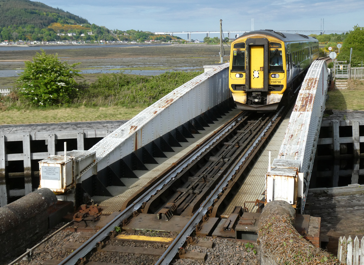 Dieseltriebzug 158716 als Lokalzug von Inverness nach Ardgay befährt in Inveness die Clachnaharry Railway Swing Bridge in der Abendsonne. Links sieht man die mechanische Verriegelung der Brücke mit dem Gestänge. Inverness, 8.5.2025