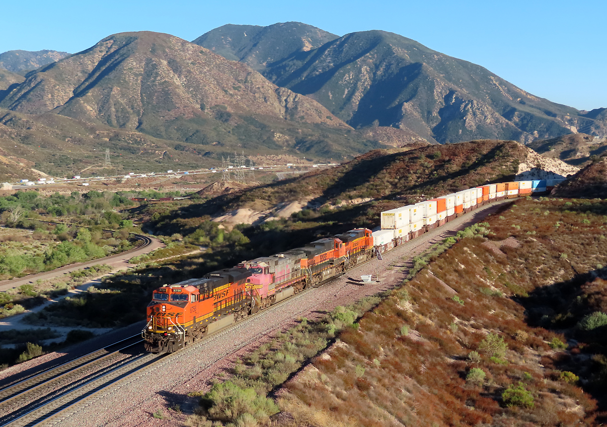 Dieser Containerzug hat vor wenigen Augenblicken die Sullivan's Curve verlassen und fährt nun Richtung Passhöhe. An 2. Stelle läuft eine Lok mit dem Warbonnet-Anstrich. Links ist die Einspurlinie mit bis zu 30 Promille Gefälle zu sehen. Ueber der Kurve in diesem Gleis sieht man noch knapp die letzten Wagen und die Schublok des Containerzuges. Cajon Pass, CA, 21.9.2022