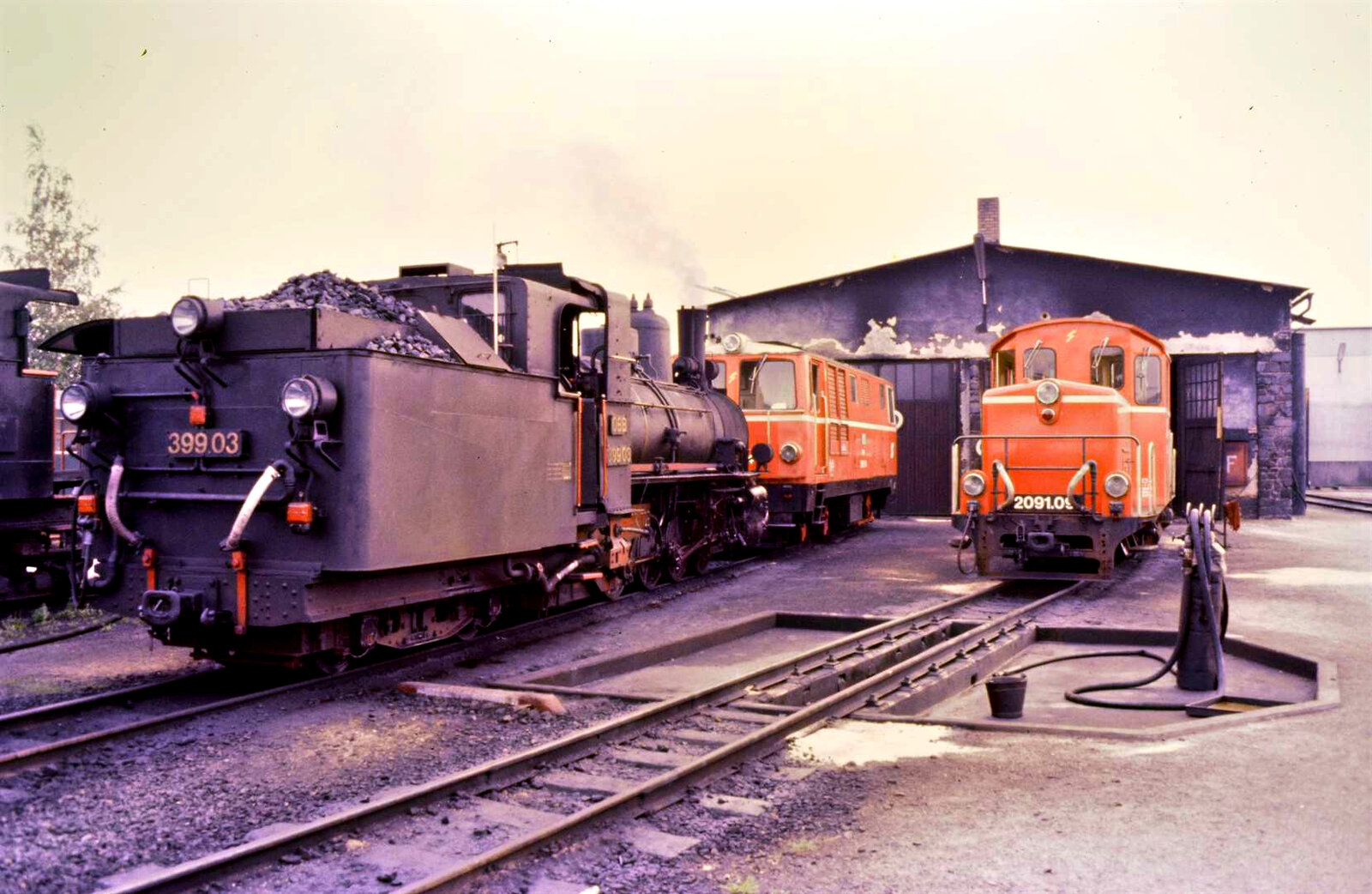 Dieses Foto vom Bw Gmünd der Waldviertelbahn entstand, als auf der Bahn noch reguläre Fahrten auch mit Dampfloks zu bestaunen waren. Vorne Dampflok 399.03 und dahinter Lok 2095.14, rechts daneben wartet Lok 2091.09.
Datum: 20.08.1984