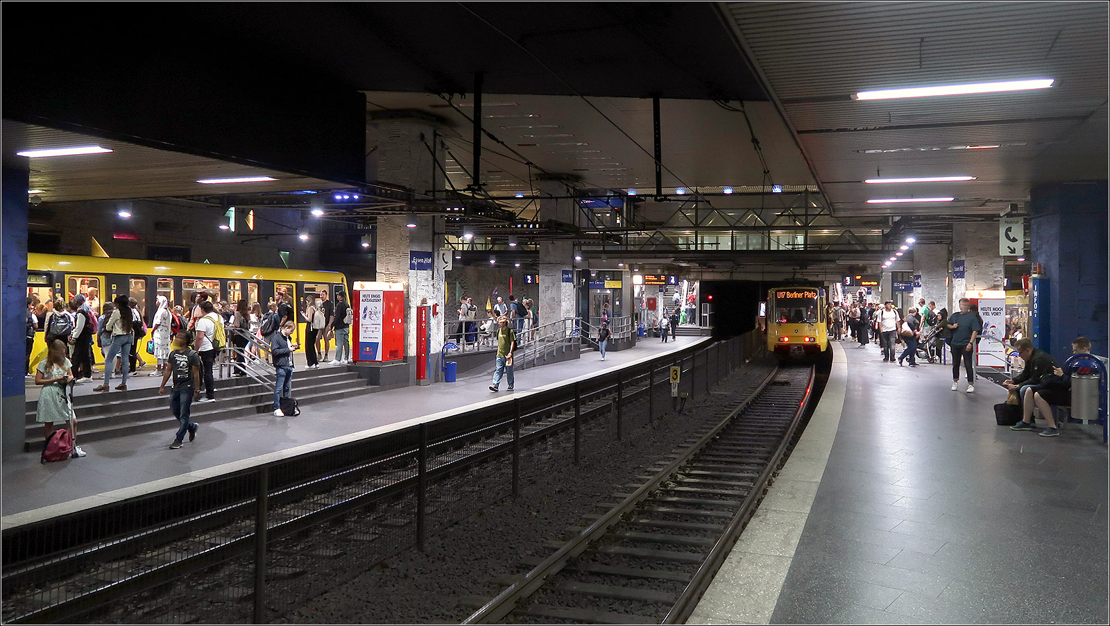 Drei Stadtbahn- und vier Tramlinien - 

... halten im viergleisigen, 1977 eröffneten U-Bahnhof Essen-Hauptbahnhof. Die beiden im Gefälle liegenden Bahnsteige sind jeweils auf einer Seite mit Hochbahnsteigen und auf der anderen Seite mit tiefen Bahnsteige versehen. An den tiefen Bahnsteigen liegen die Meterspurgleise für die Tram. Im Norden der Station trennen sich die Stadtbahn- und Tramlinien in ihre jeweilige eigene Streckenabschnitte, während im Süden sich die Strecke in drei Richtungen verzweigen, nach Westen in die Stadtbahnlinien nach Mülheim und zur Margarethenhöhe, nach Süden eine Mischbetriebsstrecke auf dreischienigen Gleisen mit der Stadtbahn zur Messe/Gruga und den Tramlinien nach Bredeney sowie nach Osten zu einer Tunnelausfahrt für zwei weitere Tramlinien.

Von der blauen Beleuchtung, die seit 1998 diese Station eine besondere Prägung gab, war bei meinem aktuellen Besuch nicht zu sehen. Ob sie Sparmaßnahmen zum Opfer gefallen ist?

23.08.2023 (M)