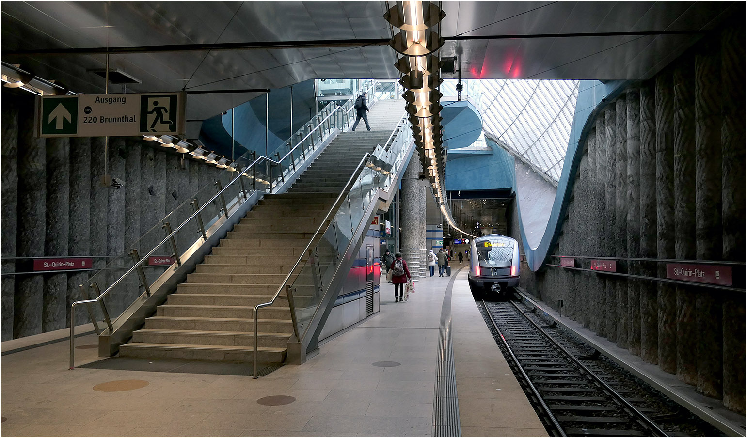 Ein besonderer U-Bahnhof in München - 

... die Station St.-Quirin-Platz an der U1-Süd. Der nördliche Zugang im Bereich der großen Deckenöffnung mit dem aufwändigen Glasdachen. Von dieser Seite ist die Eingangsebene über eine feste Treppe erreichbar.

19.02.2026 (M)