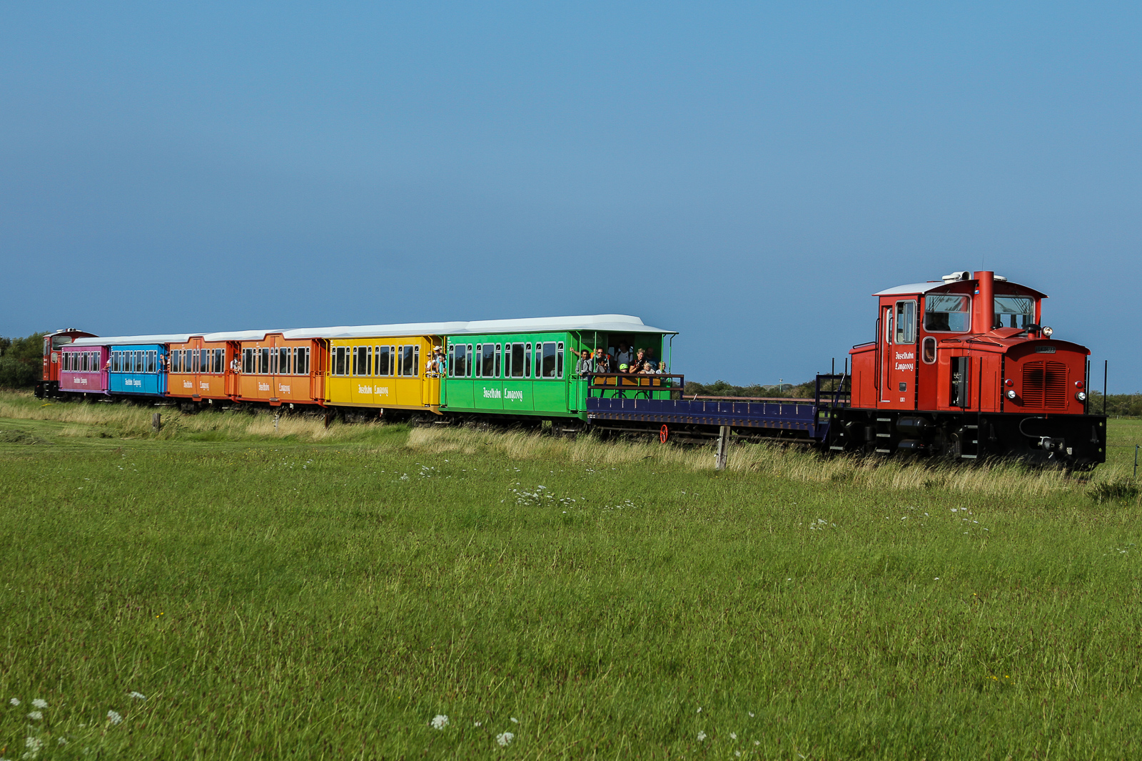 Ein Zug der Inselbahn Langeoog vom Inselbahnhof in Richtung Fähranleger.
Die Inselbahn Langeoog ist eine nicht elektrifizierte, meterspurige und eingleisige Schmalspurbahn auf der ostfriesischen Insel Langeoog. Sie wird vom Eigenbetrieb Schiffahrt der Inselgemeinde Langeoog betrieben. Die Inselbahn verbindet auf 2,6 Kilometer Länge den Fährhafen mit dem Ort Langeoog. Die Fahrzeit für die Strecke beträgt etwa sieben Minuten. Die Reihenfolge der Wagen und damit auch das farbliche Erscheinungsbild der Züge ist immer Random. Leider hat das Farbbild nicht grossartig variiert während meine Aufenthalts im August 2023.