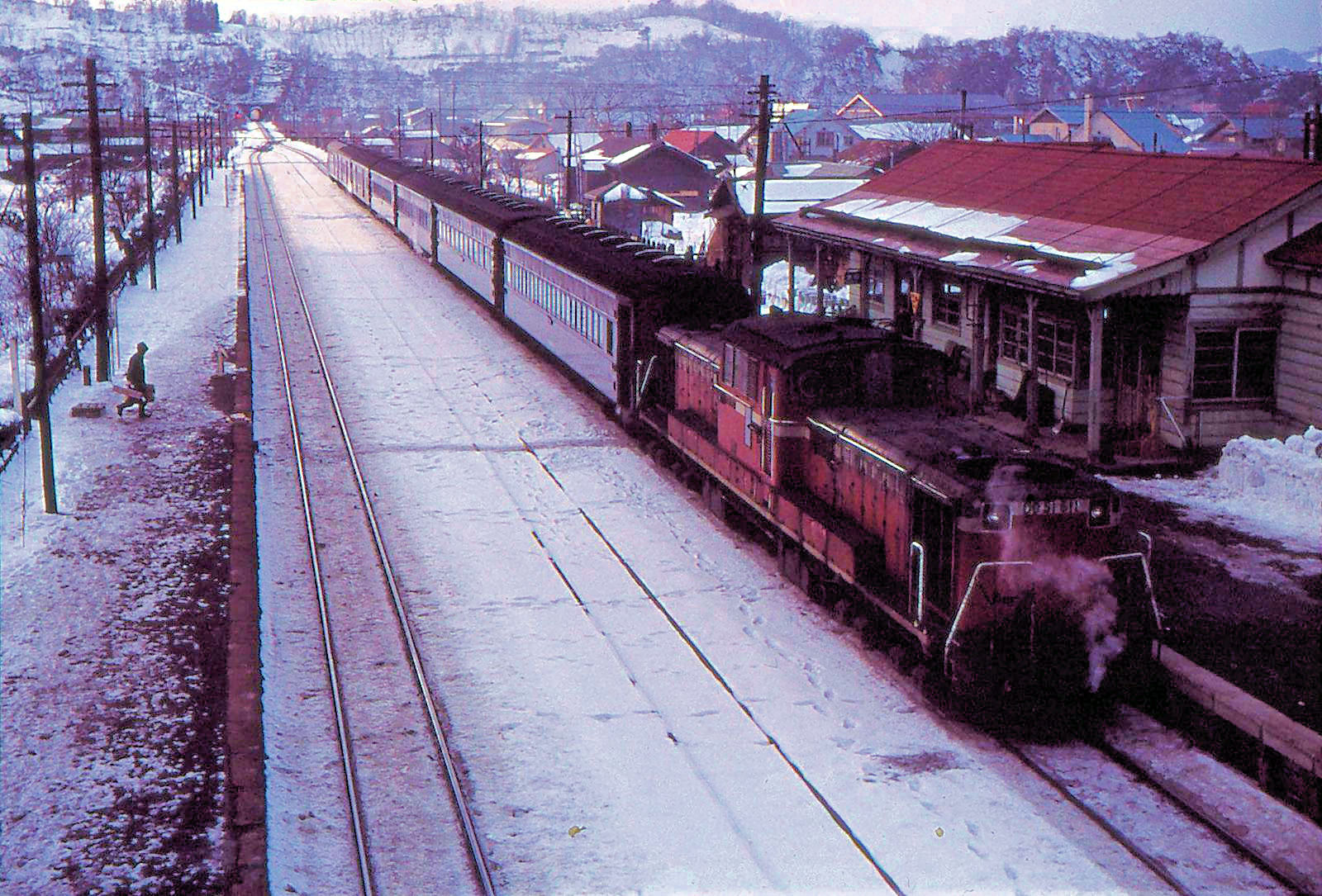 Einst fuhren viele Expresszüge vom Fährhafen Hakodate nach Sapporo über diese Bergstrecke. Hier ein Zug hinter der Diesellok DD51 611 in Ranshima, im Abstieg vom Hochplateau von Kutchan, 26.Dezember 1971 