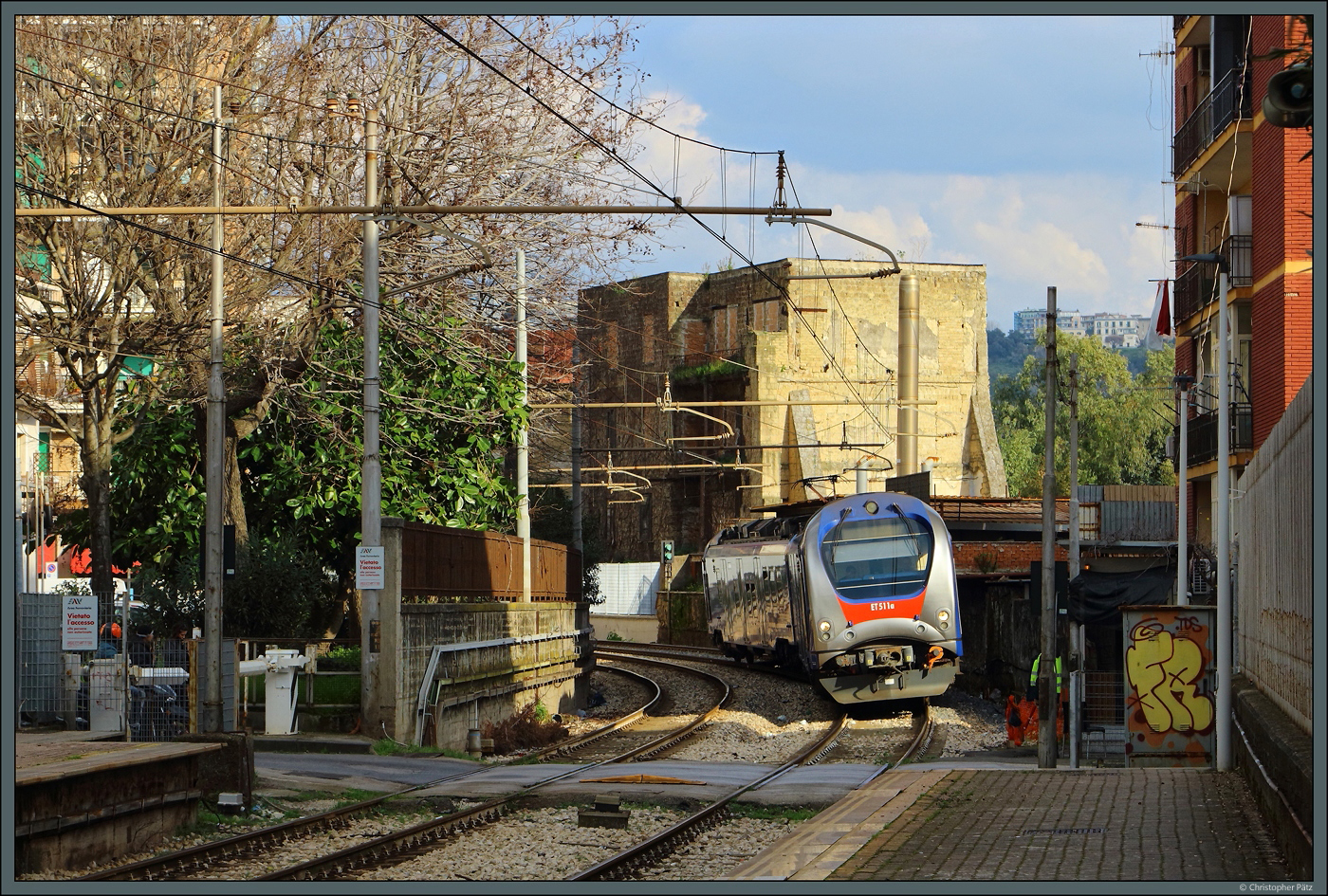 ET 511 der EAV nähert sich am 20.02.2024 durch die Häuserschluchten dem Bahnhof Bagnoli und quert dabei einen Bahnübergang.