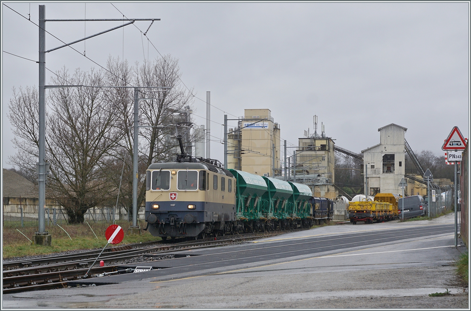 Etliche Regentropfen später kommt die IRSI/IGE  Rheingold  Re 4/4 II 11387 (Re 421 387-2) nun mit ihrem Güterzug nach Apples am Haken wieder aus dem Industrie Gelände bei Gland angefahren. 

22. Februar 2024