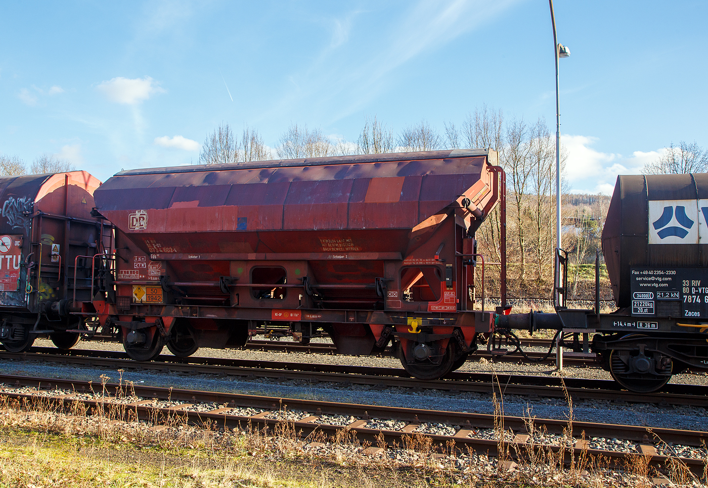 Gedeckter zweiachsiger Schüttgutwagen mit dosierbarer Schwerkraftentladung 21 80 0734 602-4 D-DB, der Gattung Tds 937, der DB Cargo AG abgestellt, im Zugverband eines Übergabezuges der KSW, am 21.02.2023 in Herdorf auf dem Rbf. der KSW.

In diesen Wagen wird Ammoniumnitrat (Gefahrgutnummer 50/1942) zur Sprengstoff Herstellung zur Fa. Dynamit Nobel Defence nach Burbach-Würgendorf gefahren (hier ist er leer). Ammoniumnitrat ist der Stoff von dem ca. 2.750 Tonnen im Hafen von Beirut am 4. August 2020 explodierten und zur der bekannten gewaltigen Explosionskatastrophe führten.

Die Wagen besitzen eine gleisseitige, dosierbare Entladeeinrichtung. Ein Innenanstrich erhöht bei den meisten der Fahrzeuge den Gebrauchswert, insbesondere durch den Schutz vor Verunreinigungen, Möglichkeiten des Transportes von Lebensmitteln, günstigeres Entladeverhalten (Rutschverhalten) bei schwer fließenden Gütern sowie durch verbesserten Korrosionsschutz bei aggressiven Ladegütern.

Der Wagen ist für den Transport von nässeempfindlichen Schüttgütern aller Art, wie z. B. Salze und Düngemittel, vorgesehen. Sie besitzen eine gleisseitige, dosierbare Entladeeinrichtung. Ein Innenanstrich erhöht bei den meisten der Fahrzeuge den Gebrauchswert, insbesondere durch den Schutz vor Verunreinigungen, günstigeres Entladeverhalten (Rutschverhalten) bei schwer fließenden Gütern sowie durch verbesserten Korrosionsschutz bei aggressiven Ladegütern. Der Transport grobkörniger oder kantiger, schwerer Güter (z. B. Kies, Schlacke, Schotter) ist wegen einer möglichen Beschädigung der Innenbeschichtung nicht zulässig.

Das Untergestell und der Wagenkasten sind als Schweißkonstruktion unter Verwendung von Walzprofilen und Blechen hergestellt. Beide Teile sind miteinander verschweißt. Der Wagen besitzt zwei Bühnen, die von beiden Seiten zugänglich sind. Beide Bühnen sind mit einer Sprossenleiter versehen. Die Arbeitsbühne ist mit Handhebeln zur Betätigung der Wölbschieber, mit dem Handrad zur Öffnung des Daches und teilweise mit einer Feststellbremse und Notbremshahn ausgerüstet. Der Neigungsgrad des trichterförmigen Wagenkastens ermöglicht eine restlose selbsttätige Entladung. Die Entladung des Wagens erfolgt über Wölbschieber. Der Wagen ist mit einem einschaligen Hubschwenkdach ausgerüstet. Das Dach wird vor dem Schwenken angehoben und dann seitlich abgeschwenkt, wobei die gesamte Breite der Beladeöffnung freigegeben wird. Im geschlossenen Zustand ist das Dach gegen unbeabsichtigtes Verschwenken gesichert.

TECHNISCHE DATEN:
Spurweite: 1.435 mm
Achsanzahl: 2
Länge über Puffer: 9.640 mm
Achsabstand: 6.000 mm
Laufraddurchmesser: 1.000 mm (neu)
Wagenhöhe: 4.198mm
Größe der Beladeöffnung Länge x Breite: 8.000 x 1.200 mm
Laderaum: 38 m³
Eigengewicht: 13.200 kg
Höchstgeschwindigkeit: 100 km/h (beladen) / 120 km/h (leer)
Maximales Ladegewicht: 26,5 t ab Streckenklasse C
Kleinster bef. Gleisbogenradius: 35 m
Bauart der Bremse: KE-GP (LL)
Bremssohle: IB 116
Intern. Verwendungsfähigkeit: RIV