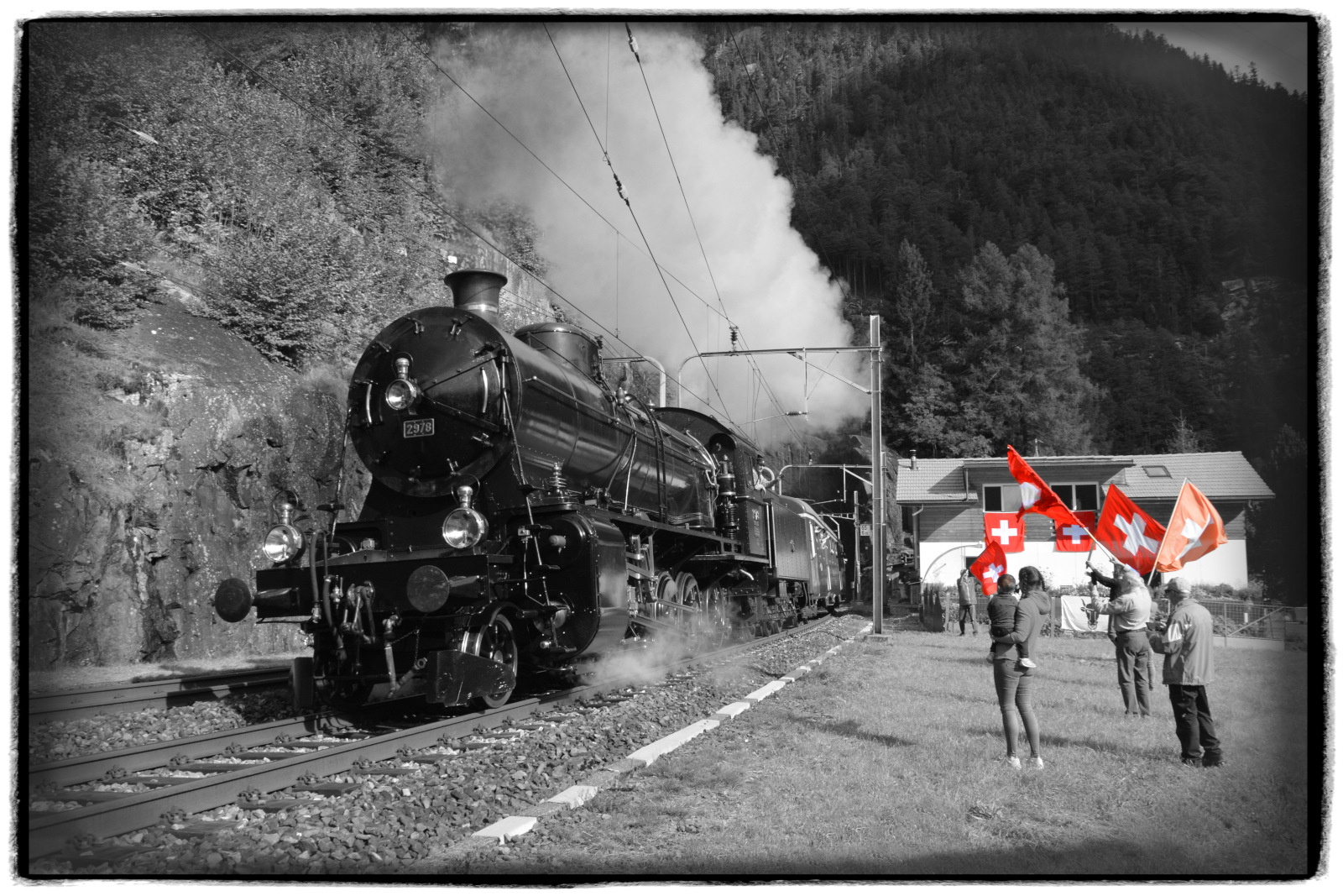 GOTTHARD-BAHNTAGE 2025: Der  Elefant  C 5/6 2978 (SBB Historic) stampft am 13.09.2025 mit Volldampf und dem Extrazug oberhalb von Wassen am Fahnenschwinger Xaver Andermatt und seinen Freunden vorbei die Gotthardnordrampe nach Göschenen hinauf.