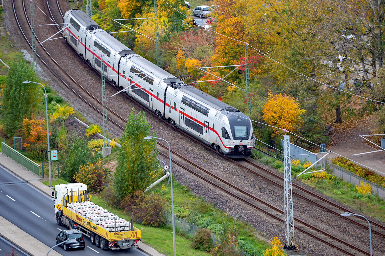 IC der BR 4110 (4116)  einfahrend in den Bahnhof Waren (Müritz), parallel dazu werden durch einem Spezial Transport per Strasse neue Schwellen transportiert. - 26.10.2022 - Versuch eines Mitzieher vom Turm St.Marien.


