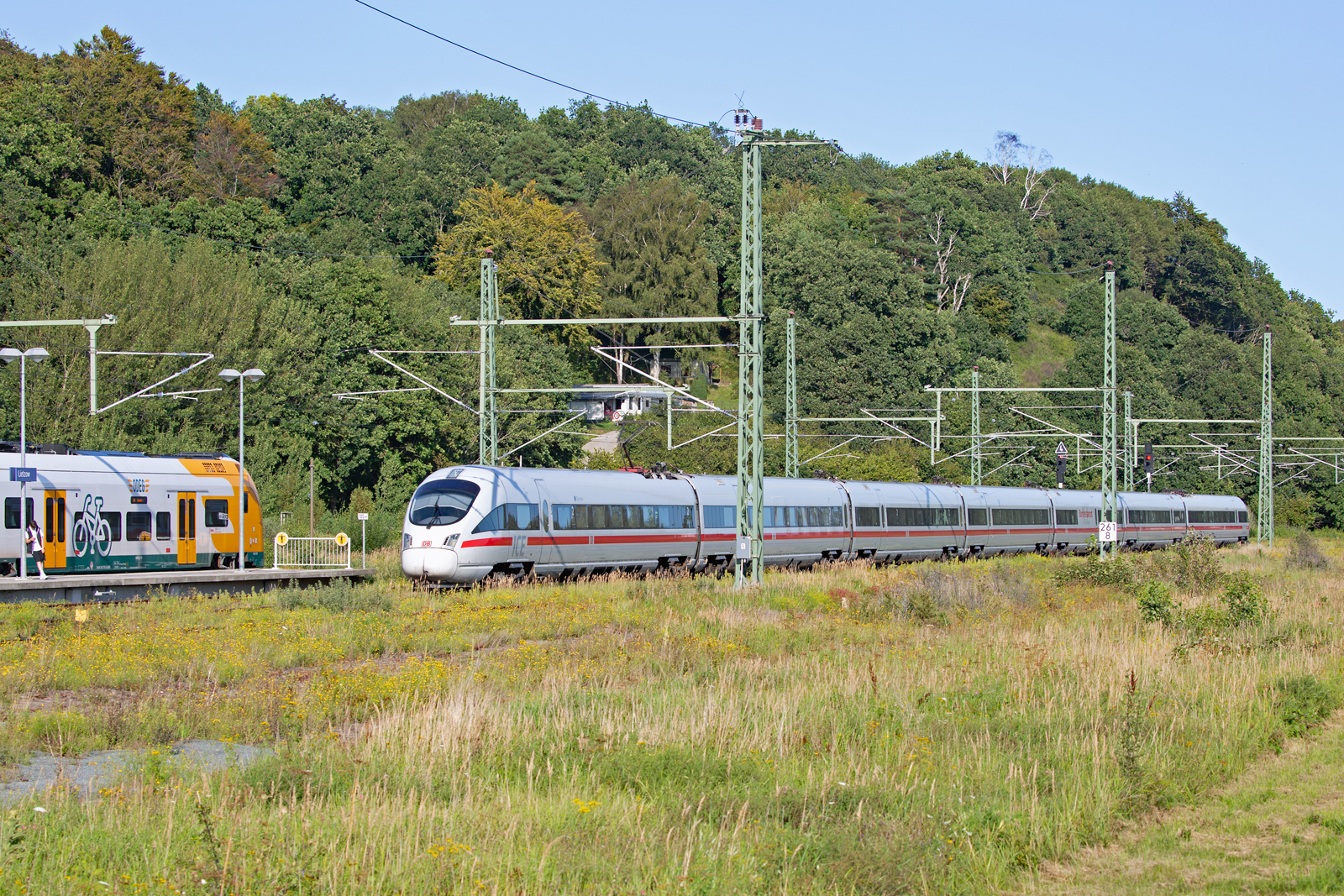 ICE GÜSTROW durchfährt den Bahnhof Lietzow nach Binz. Auf dem Nachbargleis (Bahnsteiggleis) wartet der ODEG Triebwagen nach Sassnitz  und ein Reisender, entspannt unter dem Bahnhofsschild, auf den Regio Anschluss zum Ostseebad Binz. 20.08.2023
