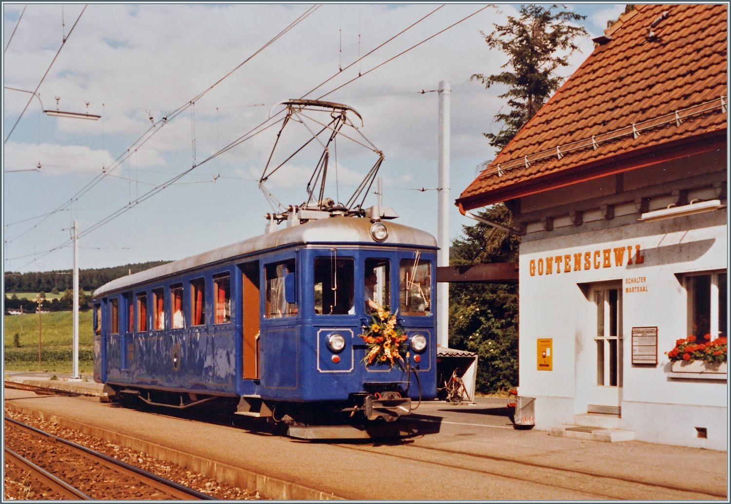 In Gontenschwil steht der WSB Bse 4/4 116. Der edle Salontriebwagen hat eine interessante Geschichte hinter sich, die ich zeitlich weit übers Bild hinaus bis in unser Tage kurz skizieren möchte: 

1901 wird der Triebwagen als CFe 2/4 N° 3 bei der AS (Aarau - Schöftlandbahn) in Betrieb genommen. Damals besass der Treibwagen Lyrastromabnehmer. Drei Jahre erhält der Triebwagen infolge der Zusammenarbeit mit der WTB (Wyentalbahn) die Nummer 16. 1932 bekommt der Triebwagen zwei weitere Antriebsmotoren und verkehrt nun als CFe 4/4 N° 16. Nach einem Zusammenstoss mit einem Güterzug 1950 wird der Triebwagen umfassend umgebaut und kommt 1952 mit einem neuen, längeren und breiteren Wagenkasten wieder in Betrieb. Durch die  Klassenreform  1959 erhält der Triebwagen die Bezeichnung BDe 4/4 16. 1962 bekommt der Triebwagen neue Drehgestelle, ein neues Getriebe und eine Schienenbremse. Mit 2 528 877 Km Laufleistung auf dem Tacho beginnt ein neuer Abschnitt in der Geschichte des Triebwagens: Nach dem Umbau in der WSB Werkstätte wird der Triebwagen als Salontriebwagen Bse 4/4 116 in Betrieb genommen und seht nun für Sonderfahrten zur Verfügung. Nach dreissig Jahren dann das scheinbare Ende: Der Bse 4/4 116 wurde 2012 ausser Dienst gestellt und zur Verschrottung abtransportiert. Aber seit 2019 kümmert sich der Verein „Pro Salonwagen WSB“ um den WSB Bse 4/4 116. Der Verein brachte den Salontriebwagen zur AVA zurück, wo er aufgearbeitet werden soll.  

Das Analogbild entstand vor gut vierzig Jahren am 14. Juli 1984 