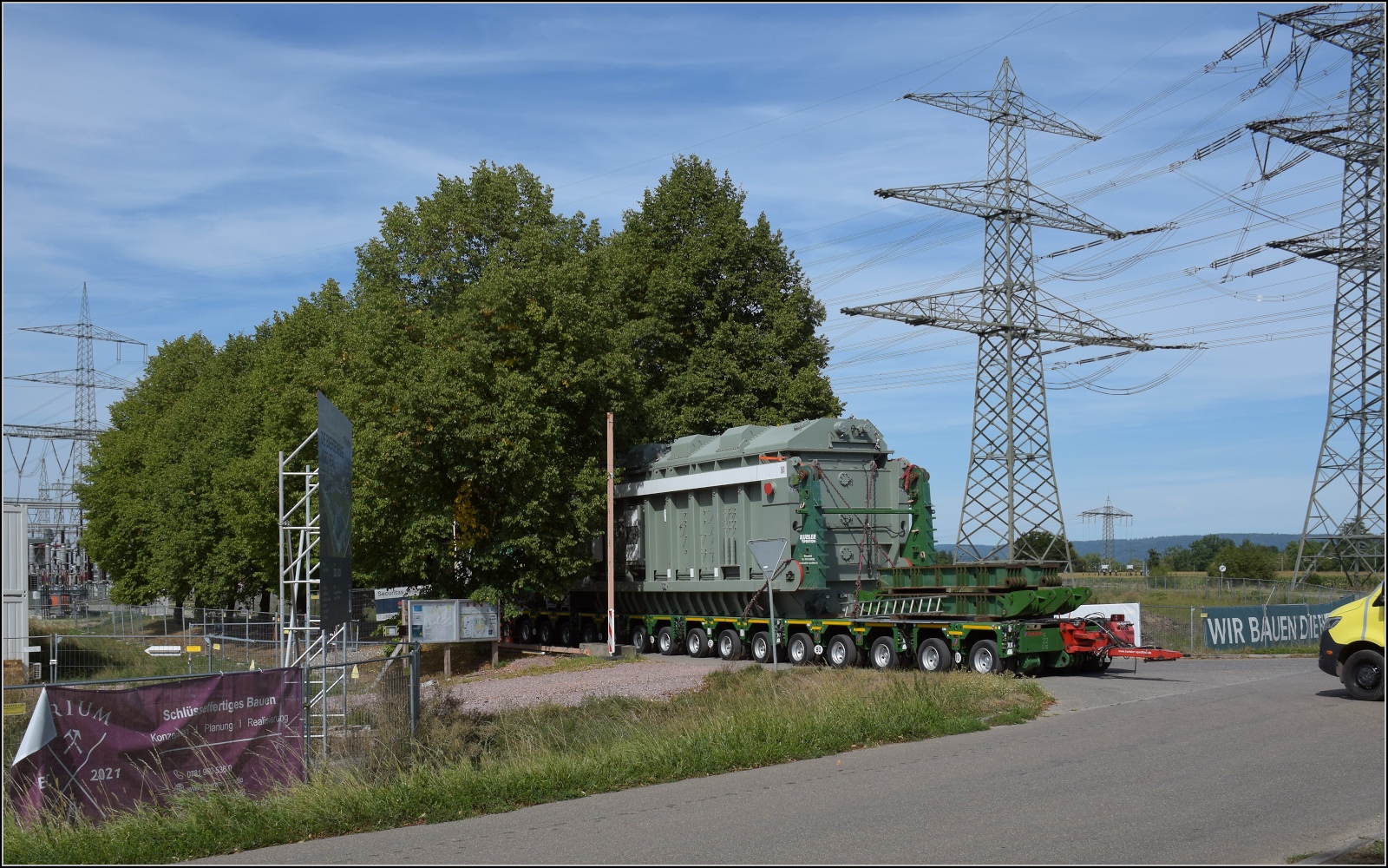 Letzte Etappe eines Schwertransports.

Weiter wurde das Trafo-Monster ganz schnell vom Bahnanschlussgleis mit dem Tieflader über die Gemeindestraße ins neue Umspannwerk befördert, einen Engpass gab es noch zu bewältigen. Die Eingangsalle hatte die Zufahrt ganz schön eingeschränkt. Da musste auch die Werksleiterin ordentlich um ihre Bäume zittern und fotografierte neben mir den Transport.  September 2022.