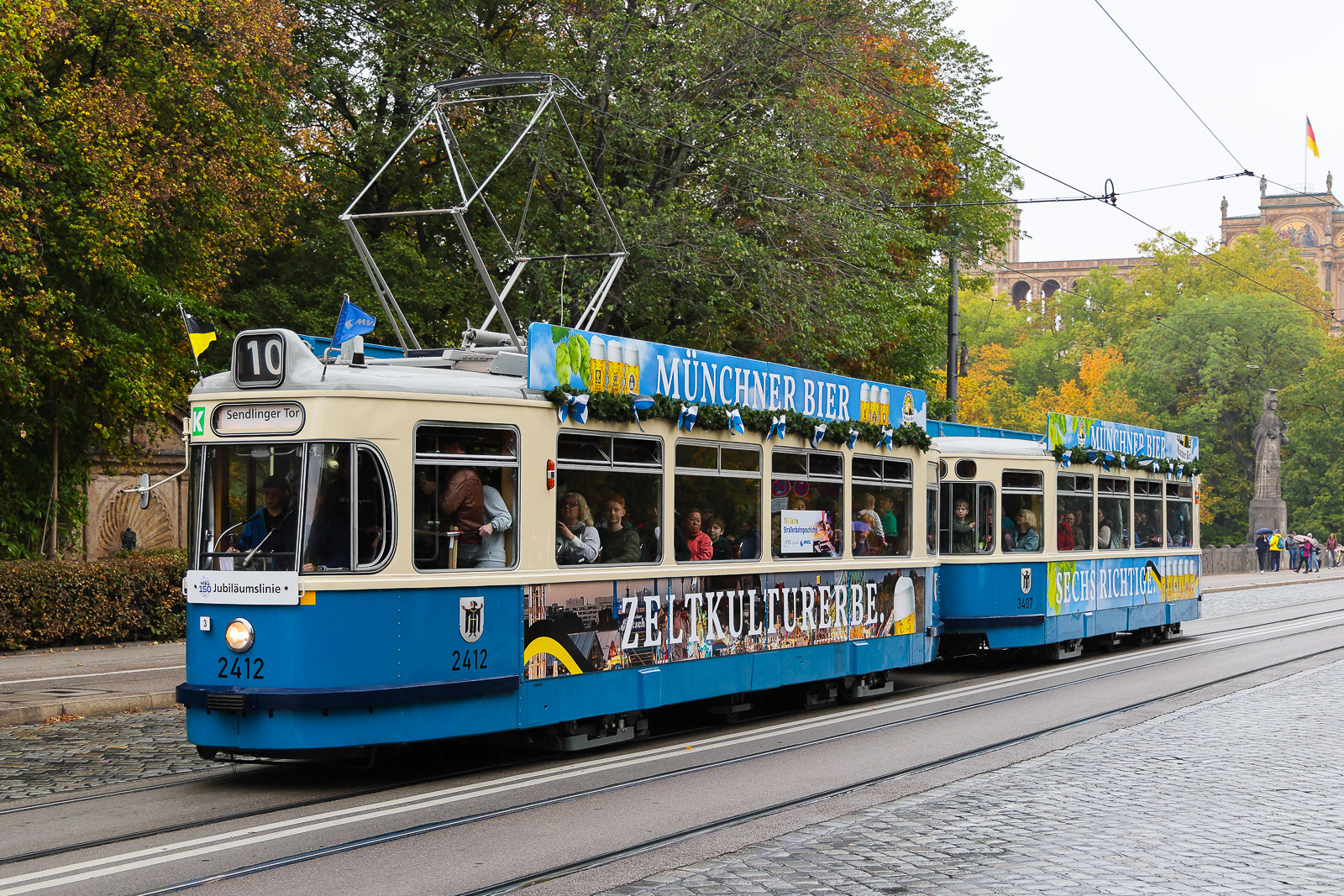 M4-Zug 2412/3407 auf der Maximilansbrücke mit der köstlichen Bierwerbung fährt nun seine Runden Richtung Sendlinger Tor zum 150 Geburtstag der Münchener Straßenbahn am 17.10.26.