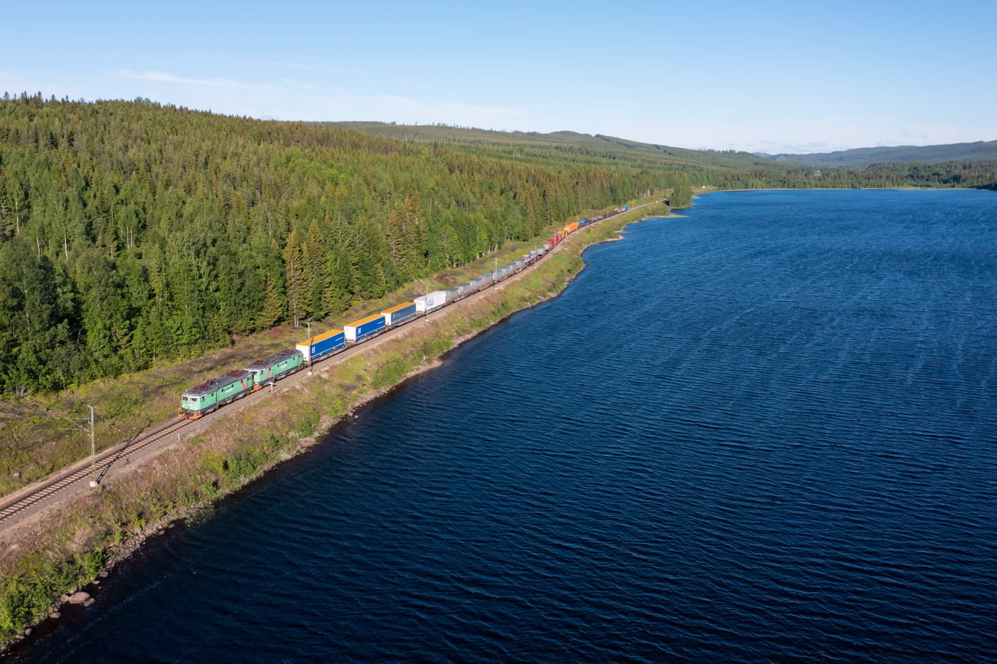 Mitten im schwedischen Wald liegt der See Stugusjön in der Nähe von Skorped. An seinem Südufer verläuft die Stambanan genom övre Norrland. Am Morgen des 15.06.2022 ist der Zug 4302 von Green Cargo mit einer Doppeltraktion Rc4 auf dem Weg nach Norden.