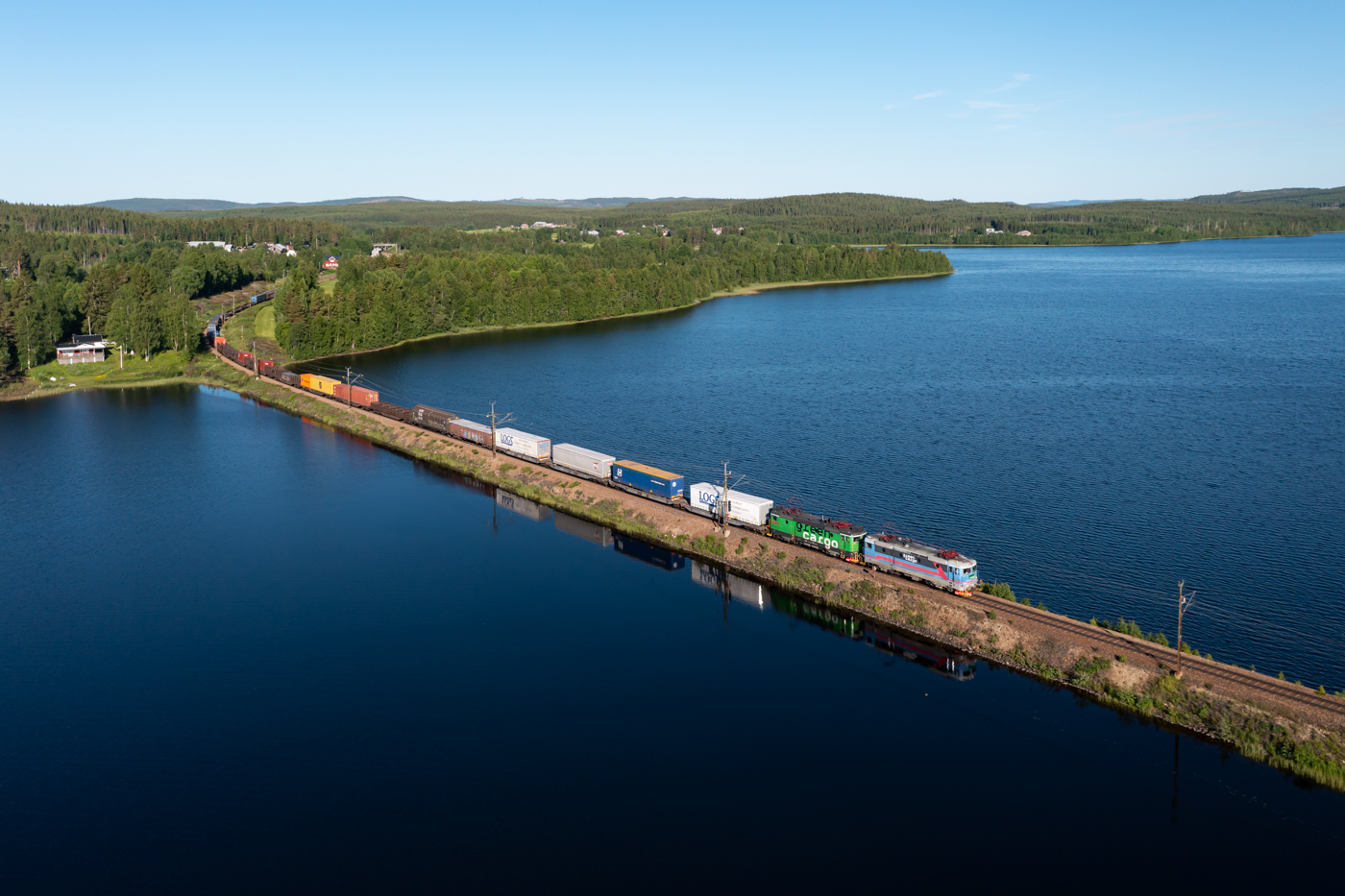 Morgens fahren auf der Stambanan genom övre Norrland mehrere Güterzüge in  dichter  Taktfolge, d.h. rund 10 Güterzüge in 4 Stunden, in Richtung Norden. Durch das Fahren in solchen Bündeln lässt sich die Leistungsfähigkeit der eingleisigen Strecke erhöhen. Nachmittags und in der Nacht fahren dann Güterzüge überwiegend in Richtung Süden. Den Anfang der morgendlichen Rushhour macht am 24.06.2022 der Green Cargo 4318, der soeben den kleinen Bahnhof Björnsjö durchfahren hat und nun den See Björnsjön überquert.
