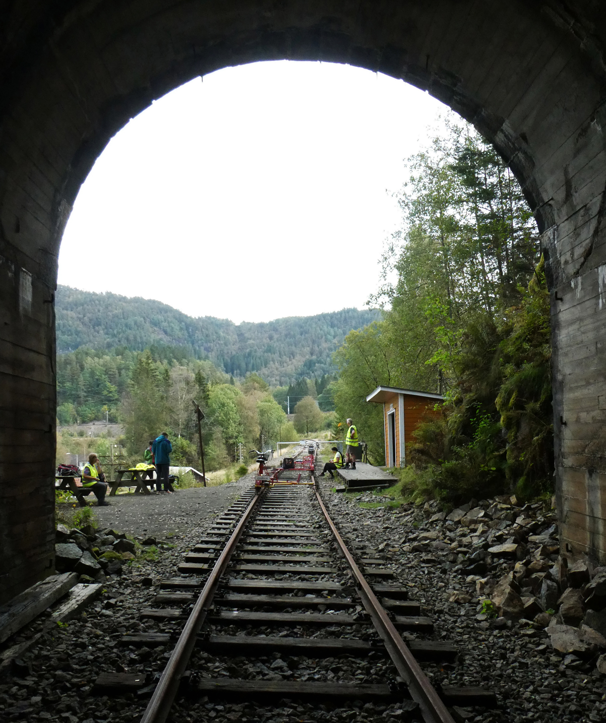 Nein, der Standort des Fotografen ist nicht gefährlich: es sind keine weiteren Schienenvelos auf der Strecke unterwegs. Blick aus dem letzten Tunnel auf die Endstation Bakkekleivi: die anderen zwei Paare warten, bis es 14 Uhr ist, dann dürfen sie die Rückfahrt nach Flekkefjord antreten. Hinter der Kurve im Hintergrund mündet das Gleis in den Bahnhof Sira an der Strecke Oslo - Stavanger. Sira, 9.9.2024