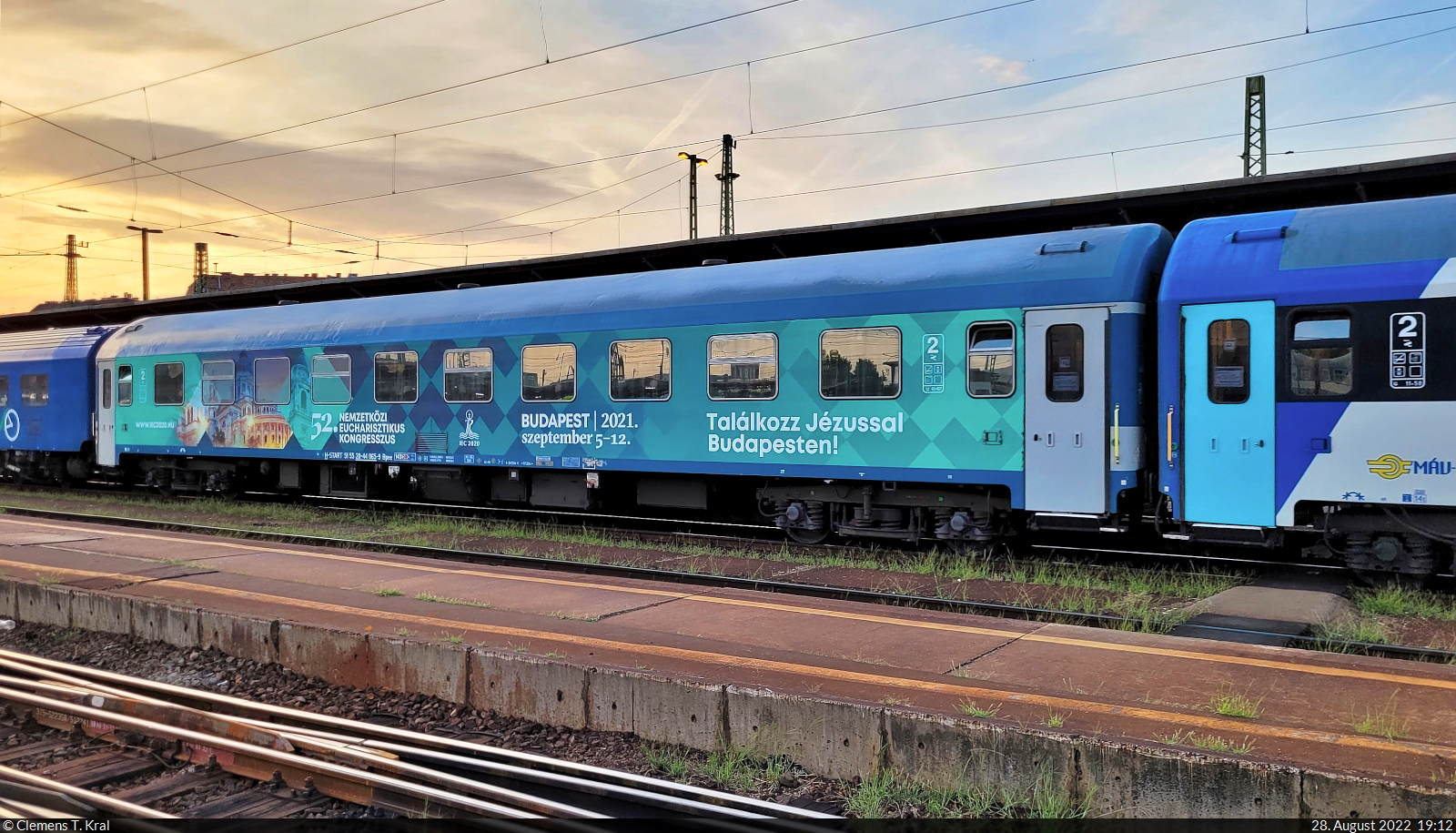 Personenwagen der 2. Klasse mit der Bezeichnung  Bpee  (51 55 20-44 065-9 H-START) bei der Einfahrt mit Zuglok 431 214-0 im Endbahnhof Budapest-Keleti pu (HU). Er wirbt für den 52. Eucharistischen Weltkongress – eine Zusammenkunft der römisch-katholischen Kirche in Budapest – der zum Aufnahmezeitpunkt bereits ein Jahr zurücklag.

🧰 MÁV
🚝 IR 19203 Szombathely (HU)–Budapest-Keleti pu (HU)
🕓 28.8.2022 | 19:13 Uhr
