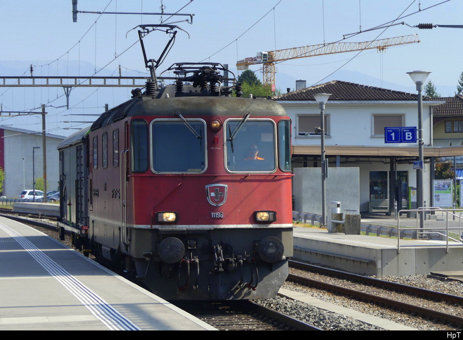 SBB - Schnappschuss der Re 4/4  420 196 mit 1 Güterwagen bei der durchfahrt im Bhf. Busswil am 12.08.2025 ... Bild wurde mit einem Natel gemacht.