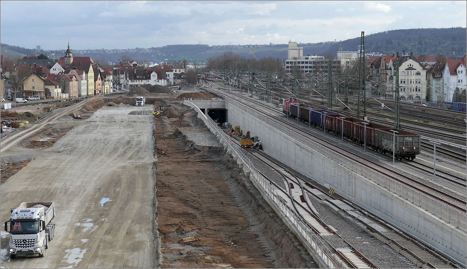 Stuttgart 21 in Untertürkheim - 

Links entsteht auf dem ehemaligen Güterbahnhofgelände der neue Abstellbahnhof als Ersatz für die Anlage beim Rosensteinpark in Stuttgart-Nord. Im Bild ist nur ein Teil der dafür vorgesehenen Fläche sichtbar. Daneben ist die Tunnelrampe der Zuführung Untertürkheim zu sehen. Die anschließenden Tunnelröhren führen unter dem Neckar hindurch, verlaufen weiter unter dem Osten von Stuttgart und erreichen den neuen Hauptbahnhof am Südkopf. Im Norden der neuen Abstellanlage wird der Hauptbahnhof über den Bahnhof Bad Cannstatt von der anderen Seite her erreicht. So können endende Zügen immer in Fahrtrichtung weiter zur Abstellanlage fahren. 

20.02.2024 (M)