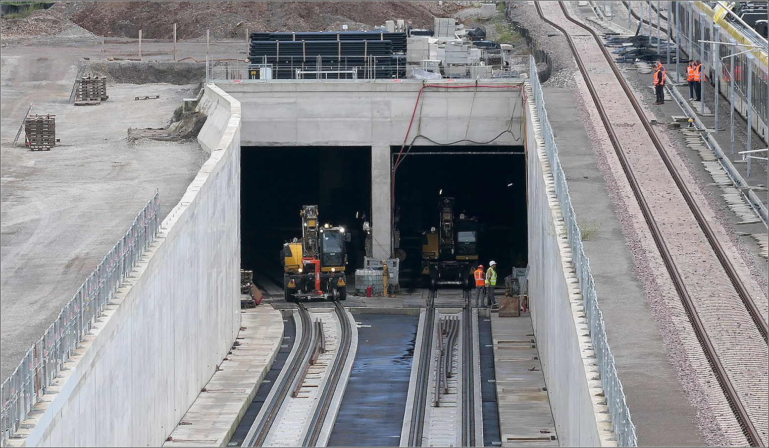 Tunneleinfahrt und Zweiwegebagger - 

Man sieht das die Gleise auseinanderlaufen, da diese dann in zwei Einzelröhren zum Stuttgarter Hauptbahnhof führen. Unter dem Neckar vereinigen sich kreuzungsfrei die beiden von der Tunnelrampe bei Obertürkheim her führenden Röhren mit den Tunnels dieses Abschnittes.

Die Ausfahrt hier dient in der Hauptsache der Verbindung vom Hauptbahnhof zum Abstellbahnhof und für wenige Züge die von der Remsbahn den Hauptbahnhof aus der Südrichtung anfahren, wie zum Beispiel der IC von Nürnberg nach Karlsruhe. Von den Regionalzügen wird meines Wissens kein Zug von hier zum Hauptbahnhof geleitet, da die eingleisige Verbindungsstrecke (Stichwort Interregiokurve) niveaugleich an die Remsbahn bei der S-Bahnstation Nürnberger Straße anschließt.

Ursprünglich waren auch Überwerfungsbauwerke von Bad Cannstatt her für eine zweigleisige kreuzungsfreie Anbindung des Abstellbahnhofes aus der anderen Richtung her vorgesehen, diese wird aber wohl nicht mehr verfolgt. Die meisten Züge, die am Stuttgarter Hauptbahnhof enden kommen eher von Norden her und können dann den Weg über diesen Tunnel nehmen. 

10.07.2024 (M)