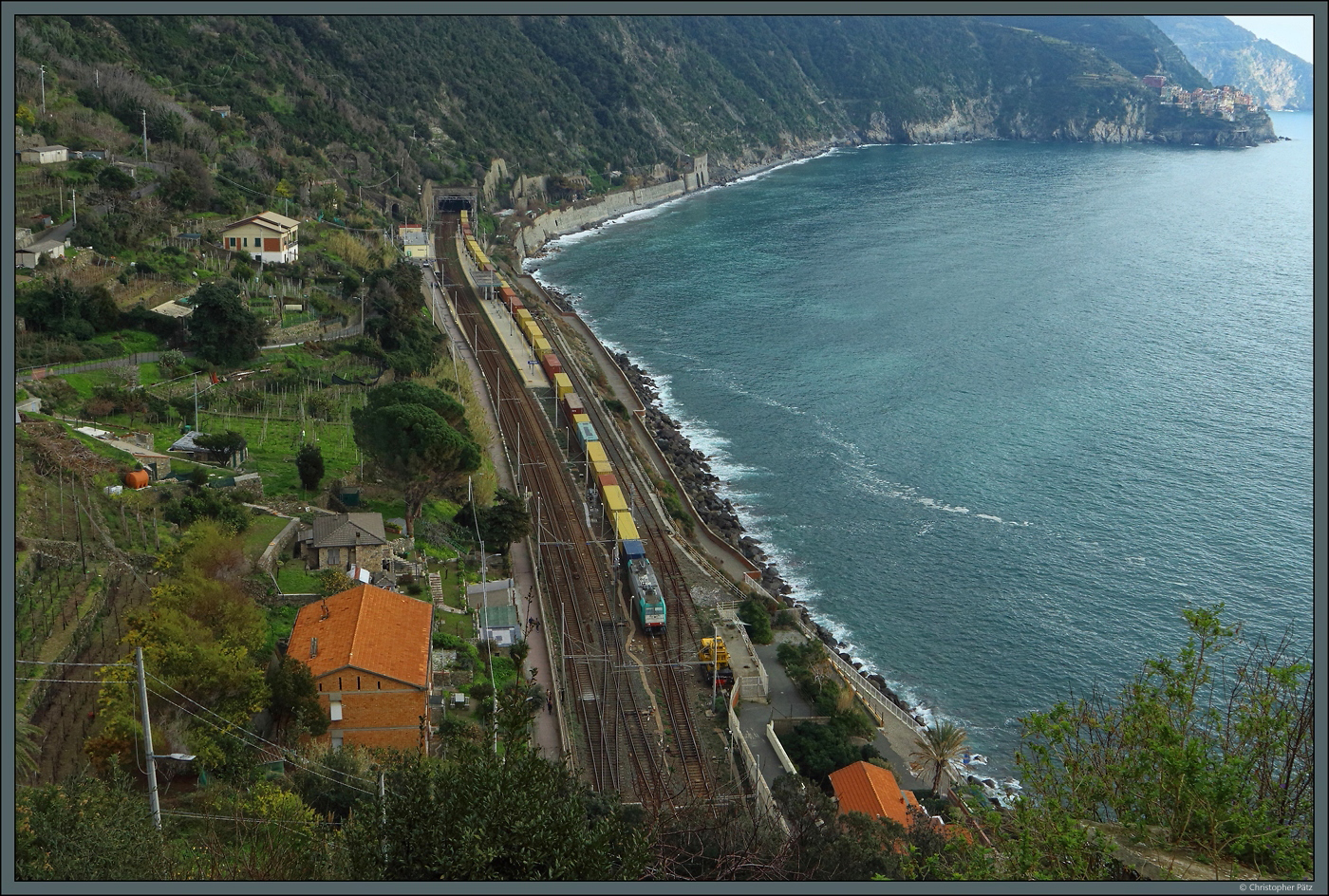Unmittelbar an der Ligurischen Küste liegt der Bahnhof Corniglia zwischen zwei Tunneln. Am 19.02.2024 durchfährt E483 010 mit einem Containerzug den Bahnhof. Rechts im Hintergrund ist das Dorf Manarola zu erkennen.