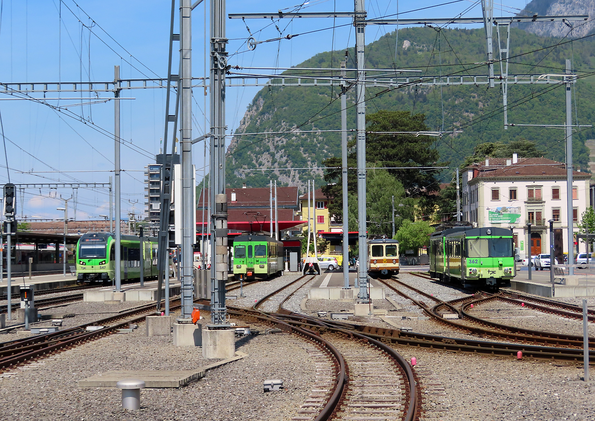 Vier Züge warten in Aigle in der Mittagsonne auf die Abfahrt: von links Regionalzug nach Champéry, Monthey, Leysin und Les Diablerets. Das Foto wurde von einem Parkplatz aus gemacht. Aigle, 2.5.2022