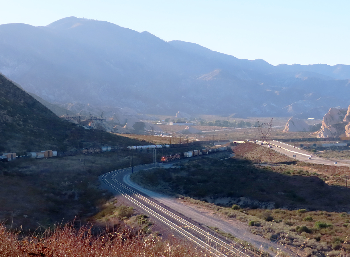 Während der gemischte UP-Güterzug im Hintergrund rechts vor den Mormon Rocks bergwärts schleicht, erscheint auf der mittleren Spur ein gemischter BNSF-Zug. Cajon Pass, CA, 21.9.2022