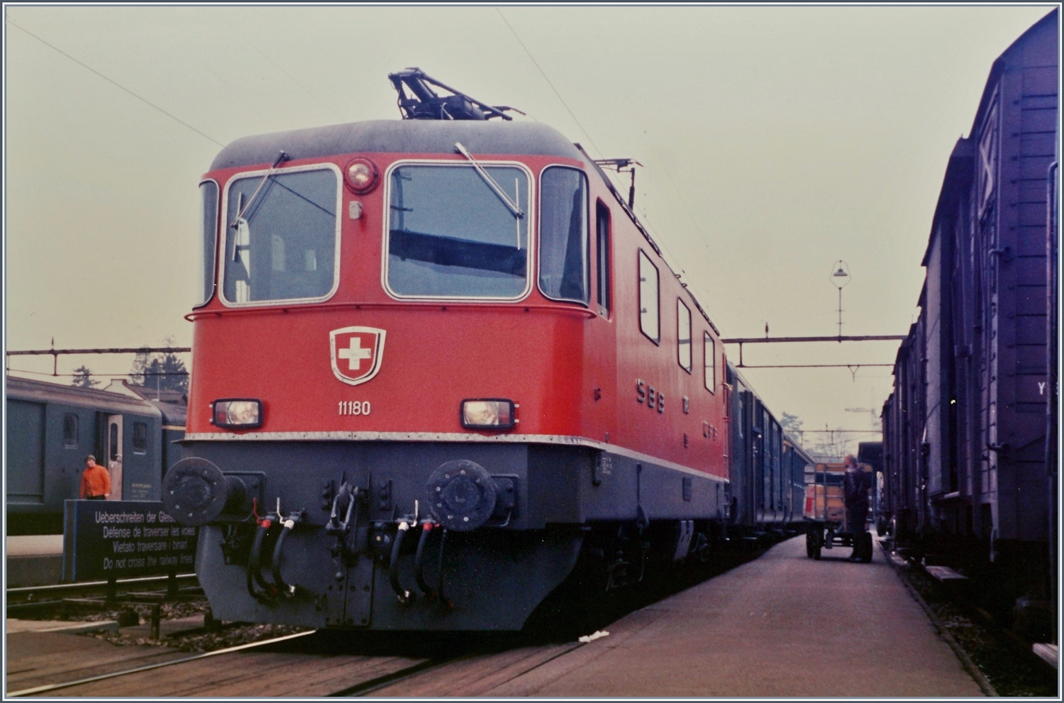 Wie bei einigen Bahnhöfen dieser Grössenordnung war auch in Aarau gleich neben dem Empfangsgebäude die Güterexpedition angesiedelt. Dadurch wurde der Hausbahnsteig in Richtung Osten recht schmal; Reisende nutzten ihn dort kaum, aber wie im Hintergrund zu erkennen ist, der Gepäckdienst. Und auch ich zwängte mich zwischen Güterwagen und Lok durch, um dieses d Szene zu fotografieren: Die SBB Re 4/4 11180 wartet mit einem Schnellzug auf die Weiterfahrt in Richtung Zürich. 

Analogbild vom März 1985