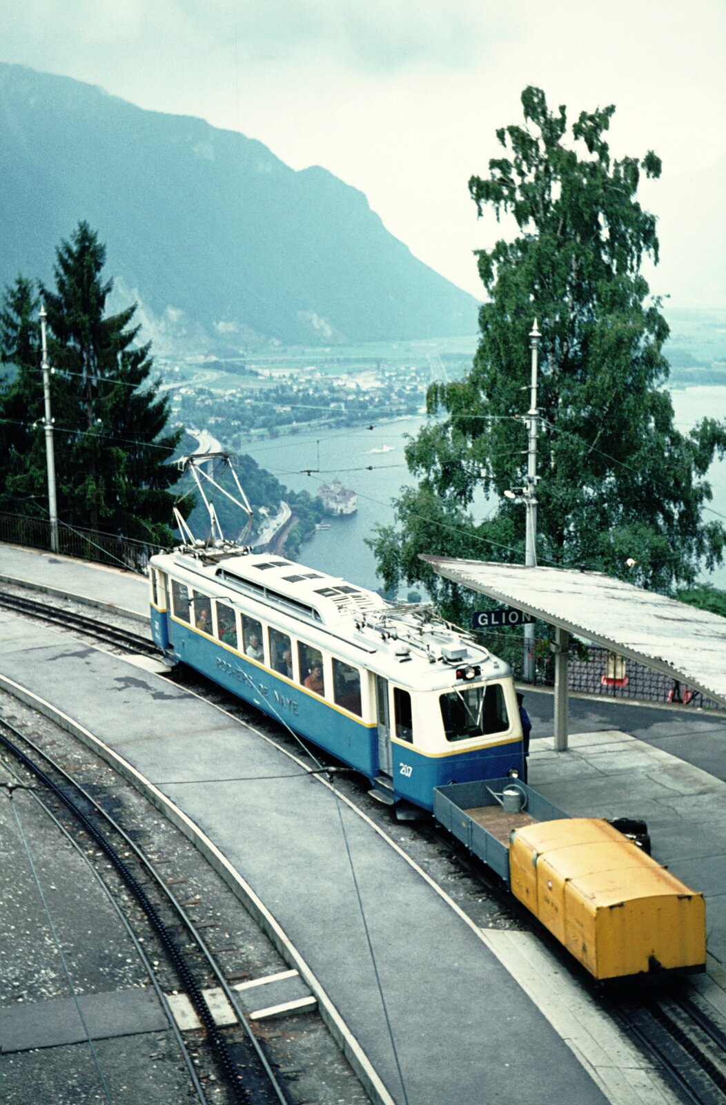Zb Rochers-de-Naye_Ausweichbhf. Glion. Tw 207 (SLM 1949) bringt die Post und eine kleine Gießkanne. Blick auf die Wasserburg Schloß Chillon. 04-09-1976 