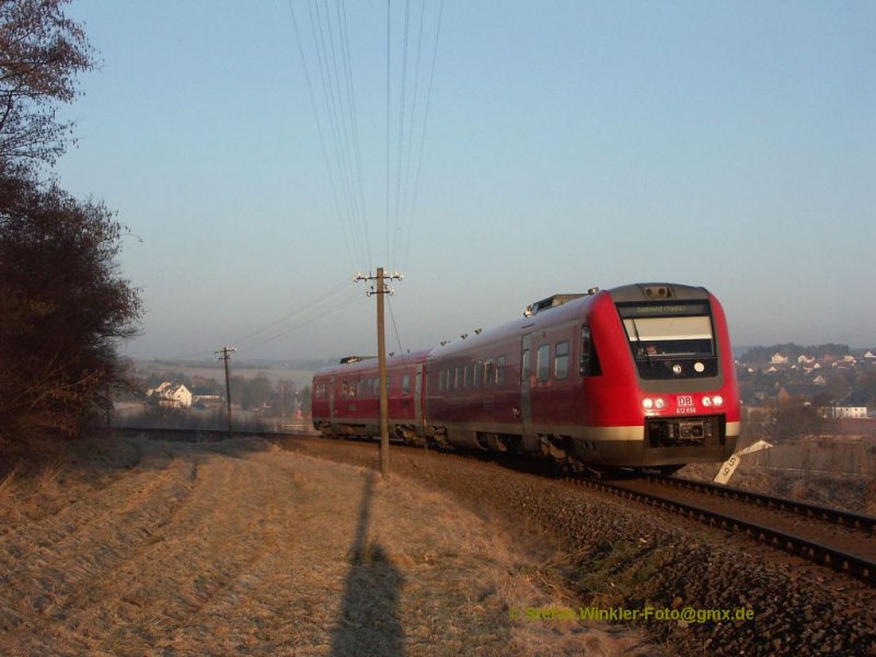 01. April 2009 oberhalb von Köditz an der Nebenbahn Hof - Bad Steben. In den ersten Sonnenstrahlen kommt der Schülerzug über die S-Kurven-Steigung Richtung Hof. Rechts hinter dem Kilometerstein und dem daneben liegenden Erdwall ist der neugebaute aber schon wieder nicht mehr bediente Gleisanschluss des Gaslagers der Fa. Leu. Glücklicherweise habe ich hier sogar mal eine Bedienungsfahrt erlebt als das noch möglich war....