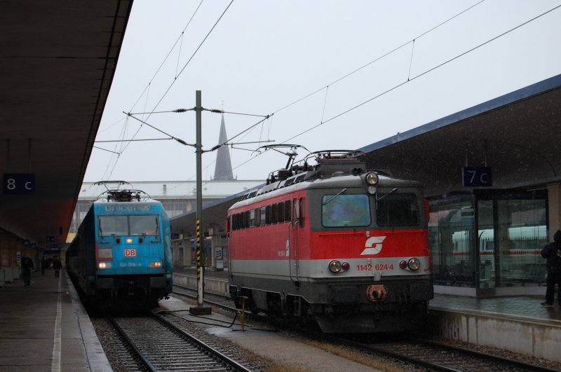 1142 642 fhrt ohne ihren CS-Zug aus dem Wiener Westbf. whrend 101 016 mit teilweise entklebter Unicef Werbung - bei der auf der rechten Seite Werbung fr Waschanlagen-Hersteller zur Herstellung einer Lokwaschanlage fr die DB Wasch mich  steht- mit ihre BB-IC nach Salzburg noch warten muss. 11.2.2009