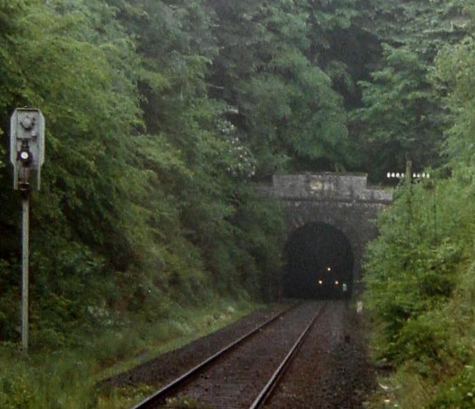 (1/3) Schienenbus Richtung Wetzlar vor der Ausfahrt aus dem Hasselborner Tunnel - der weie Fleck rechts vom Spitzsignal des Schienenbusses ist das Sdportal des gradlinig verlaufenden Tunnels, 1. Hlfte der 1980iger Jahre.