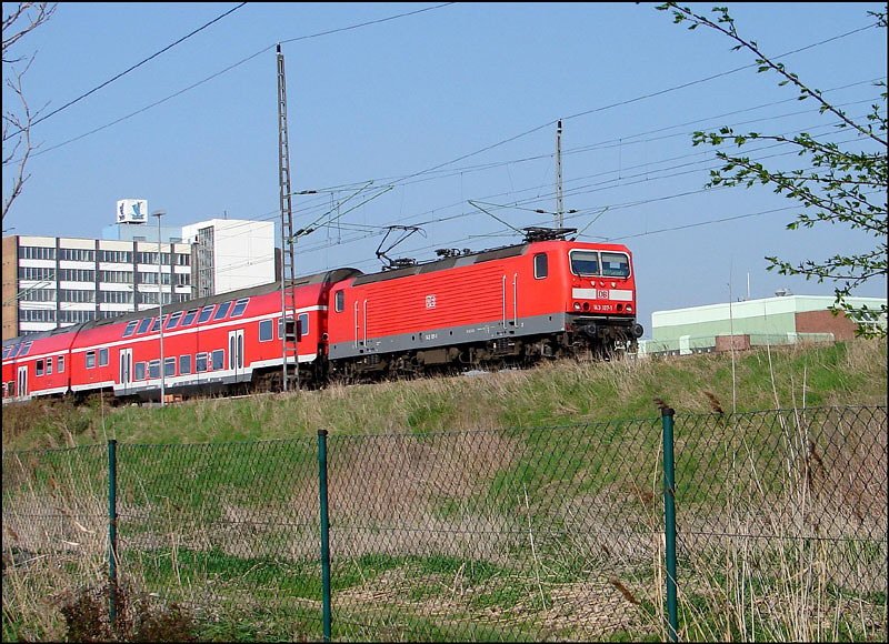 143 107-1 mit RB33326 aus Sassnitz kommend. Links im Hintergrund das ehemalige Brohochhaus der Volkswerft Stralsund. (am 04.05.06)